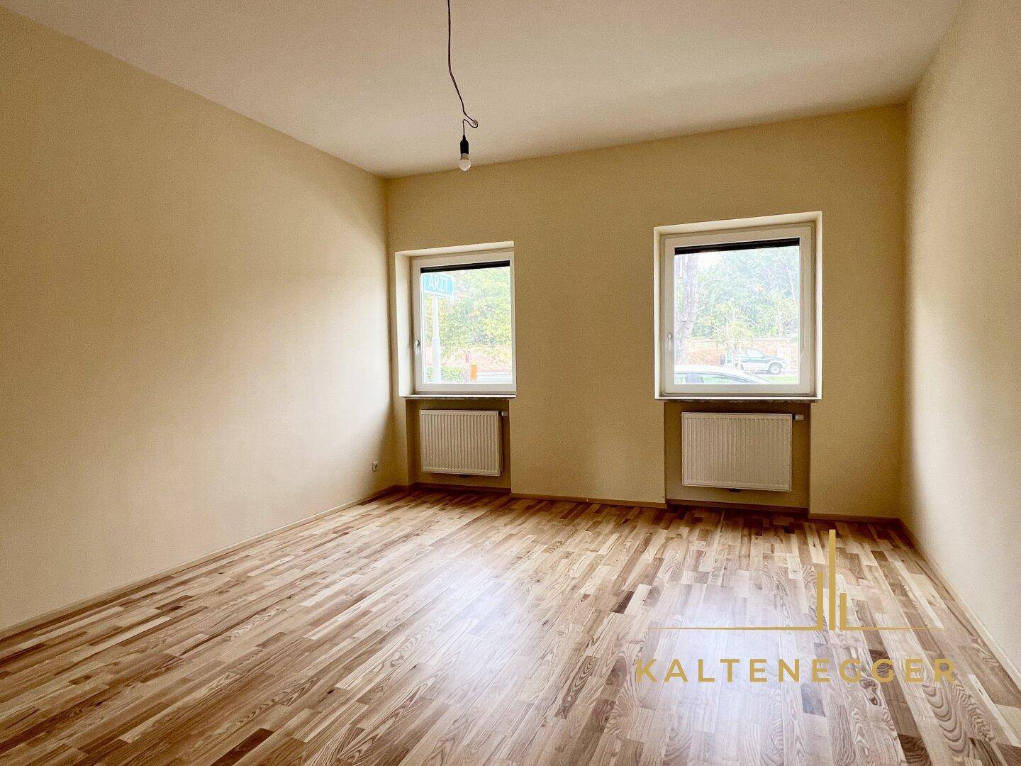Helles Zimmer mit zwei Fenstern und Parkettboden, bietet viel Tageslicht und eine angenehme Atmosphäre.