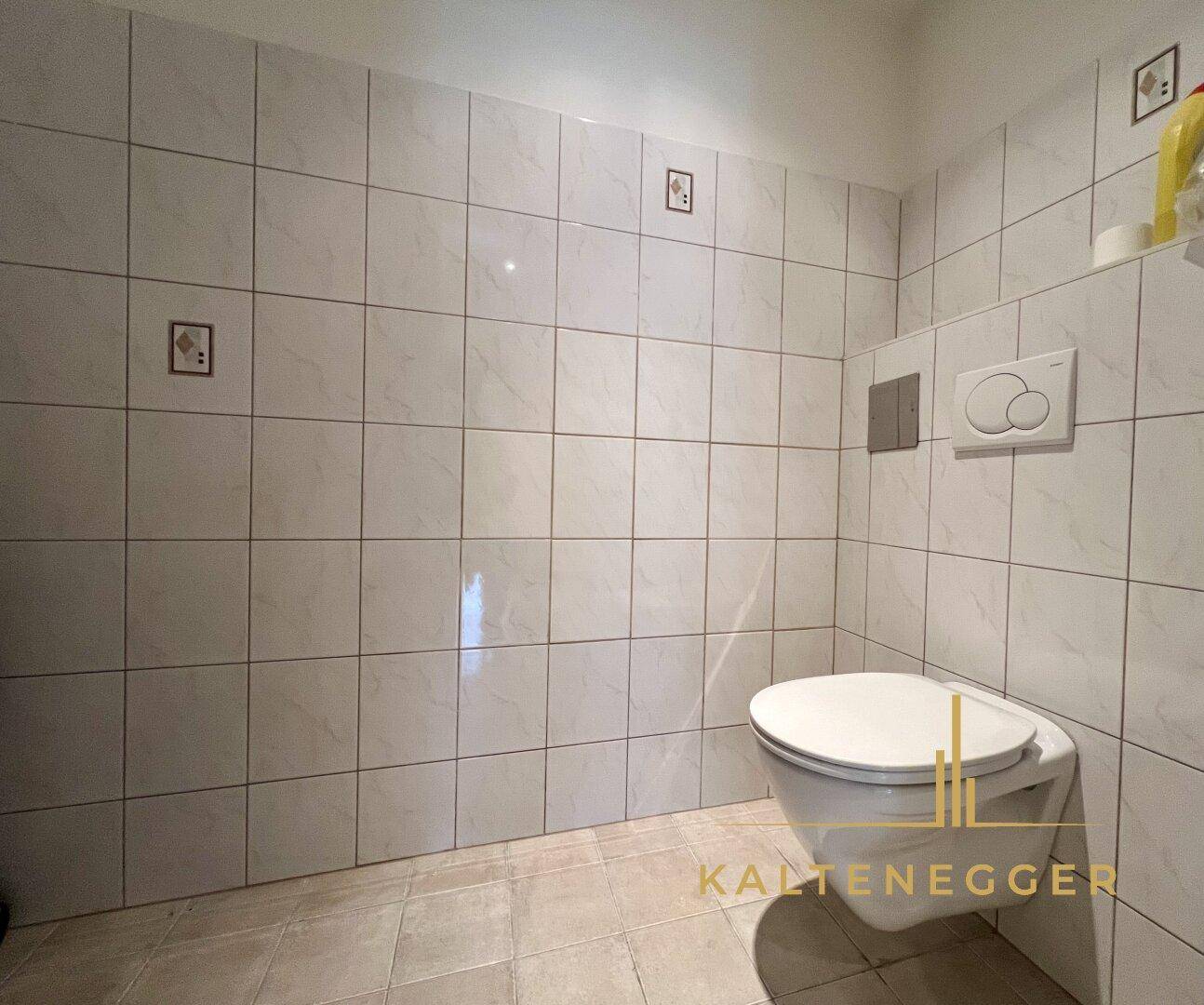 Einfaches WC mit wandhängender Toilette und hellen Fliesen, funktional und pflegeleicht.