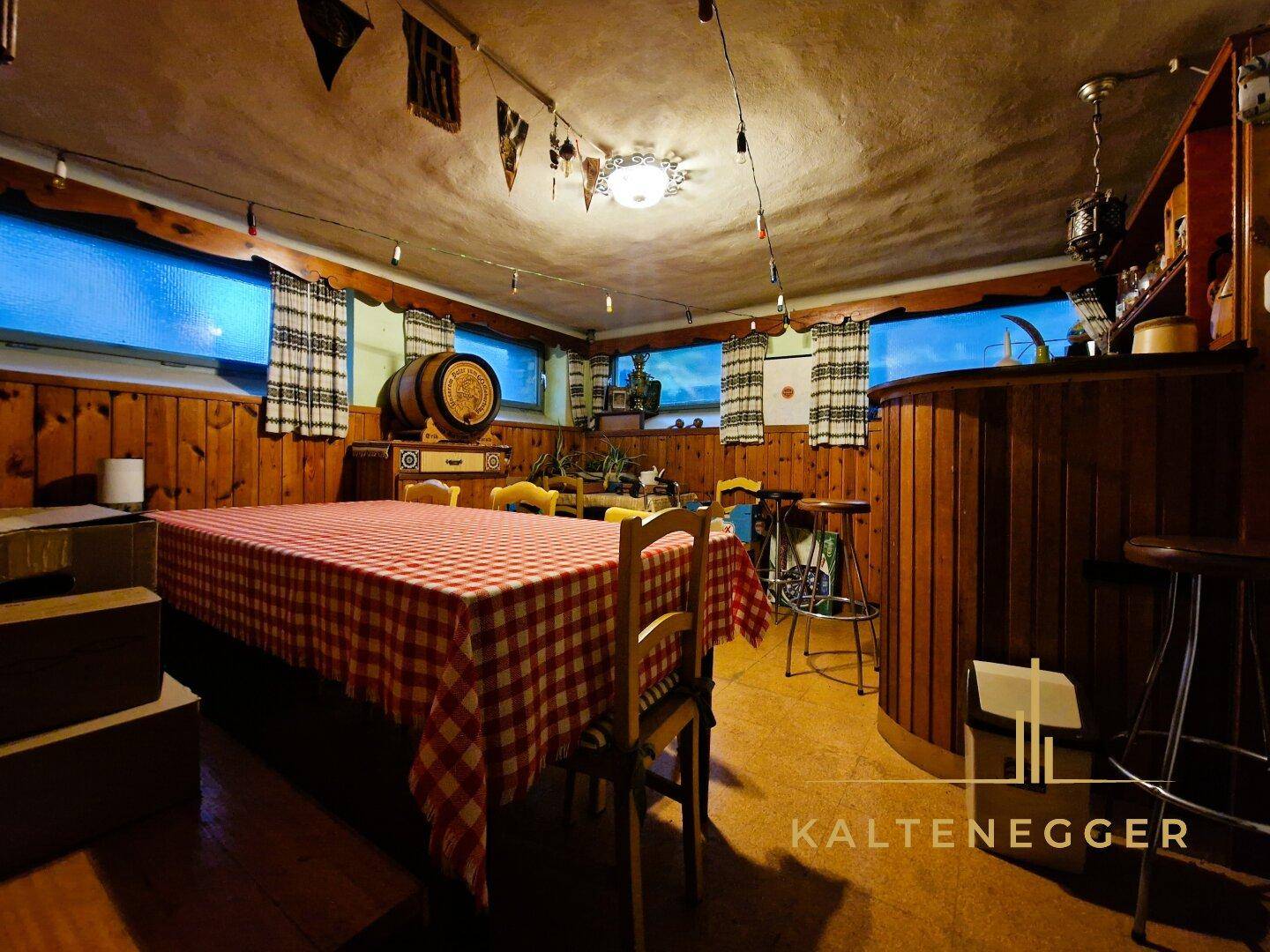 Rustikaler Partyraum im Keller mit Holzvertäfelung, Bar und großem Tisch für gesellige Abende.
