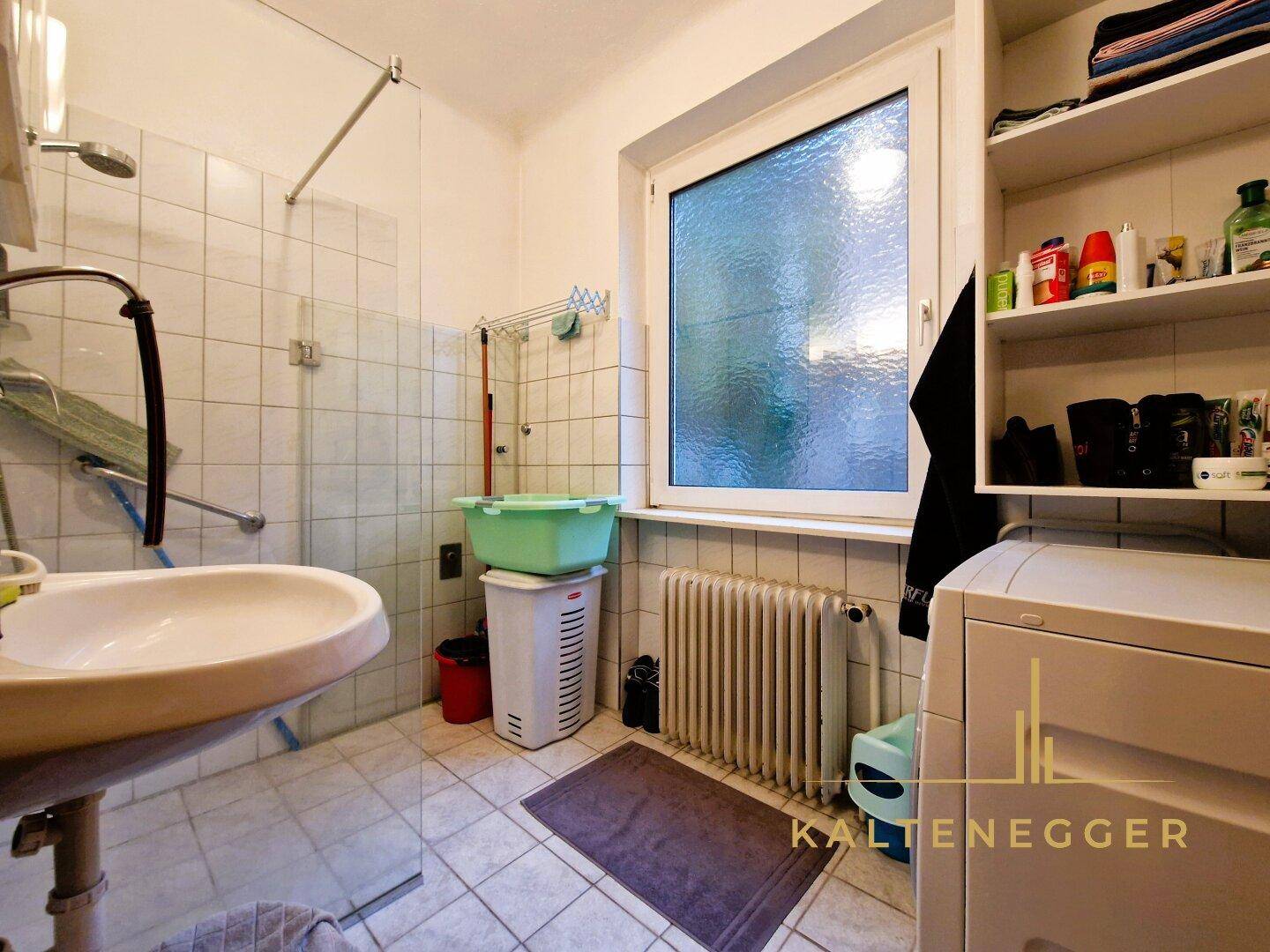 Badezimmer mit Dusche, Waschbecken, Fenster und Waschmaschine, das Renovierungsbedarf zeigt.