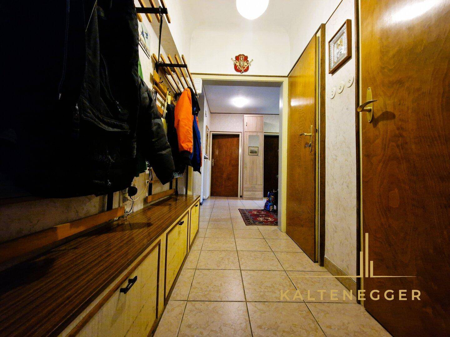Langer Flur mit Garderobe, Fliesenboden und Holztüren, der zum Eingangsbereich führt.