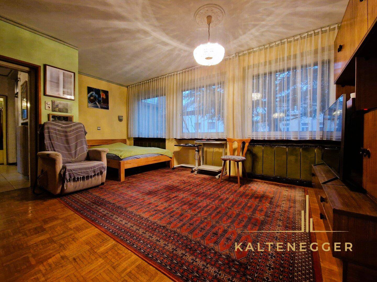 Schlafzimmer mit Parkettboden, großem Teppich und Blick nach draußen, das Renovierung benötigt.