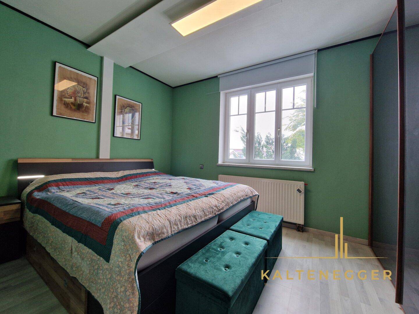 Schlafzimmer mit grünen Wänden, Doppelbett und Heizkörper unter dem Fenster.