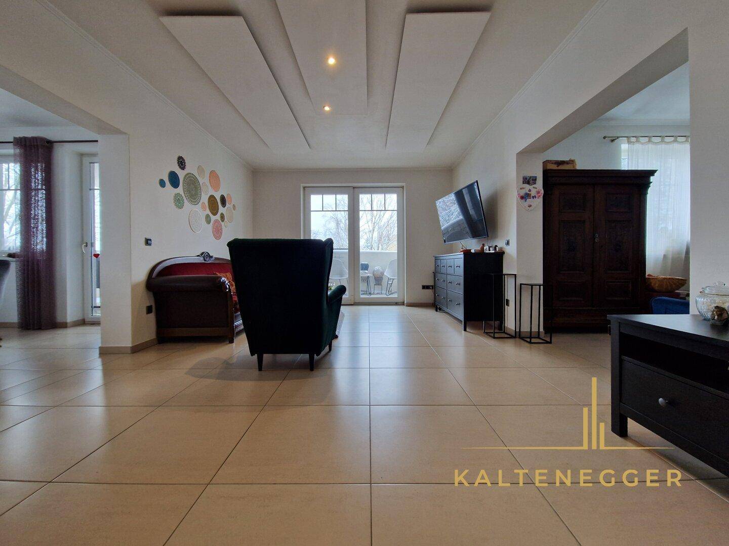 Geräumiges Wohnzimmer mit hellen Fliesen, modernen Deckenleuchten und Zugang zu einem Balkon.