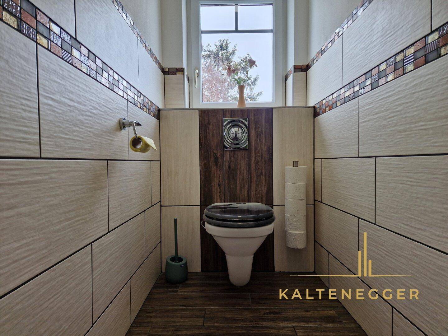 Modern gefliestes Gäste-WC mit Wand-WC und Fenster, dekoriert mit Mosaikbordüre.