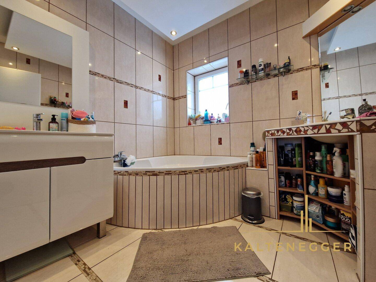 Geräumiges Badezimmer mit Eckbadewanne, hellen Fliesen und Fenster für natürliche Belüftung.