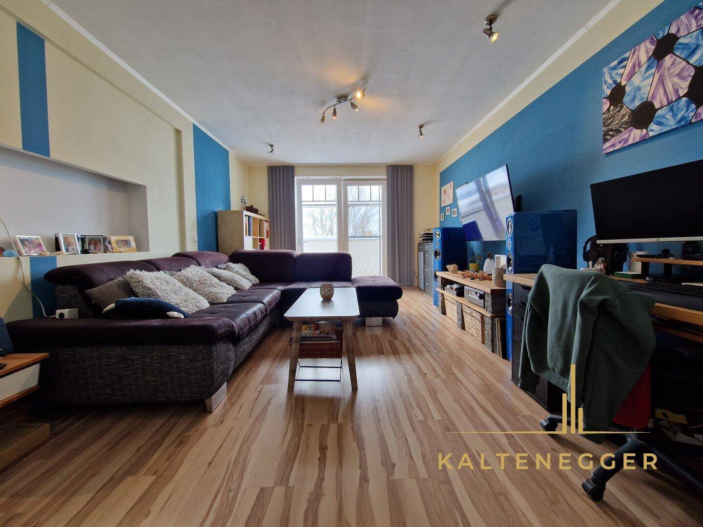 Geräumiges Wohnzimmer mit Laminatboden, blauen Akzentwänden und großem Ecksofa.