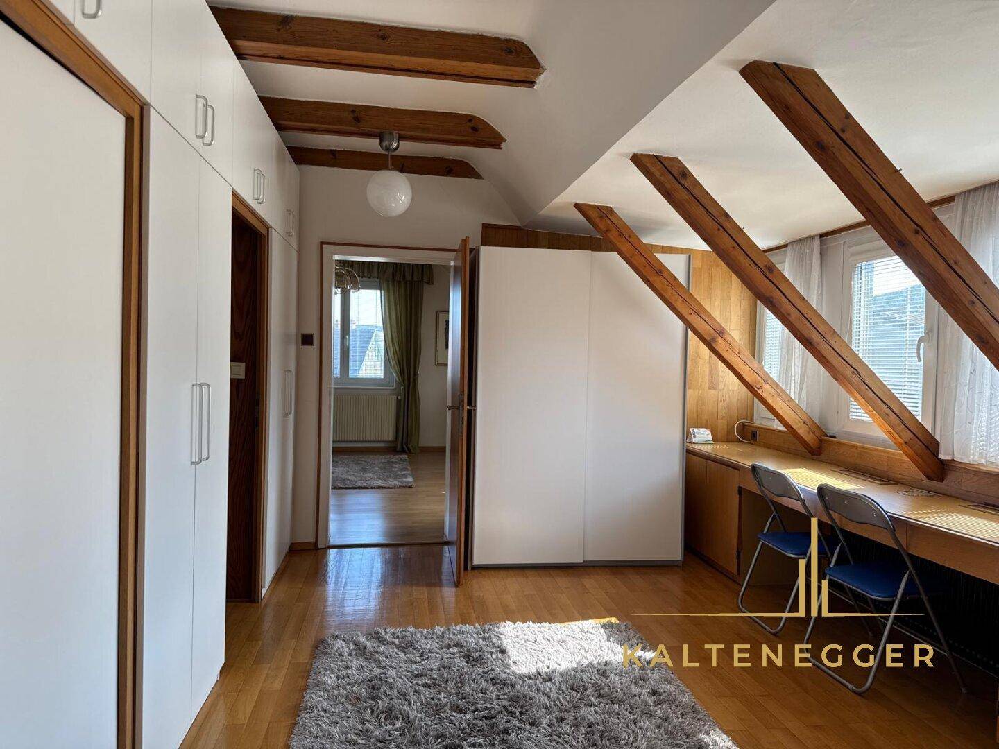 Schlafzimmer mit Einbauschränken, Holzbalken und Schreibtischbereich unter Dachschrägen.