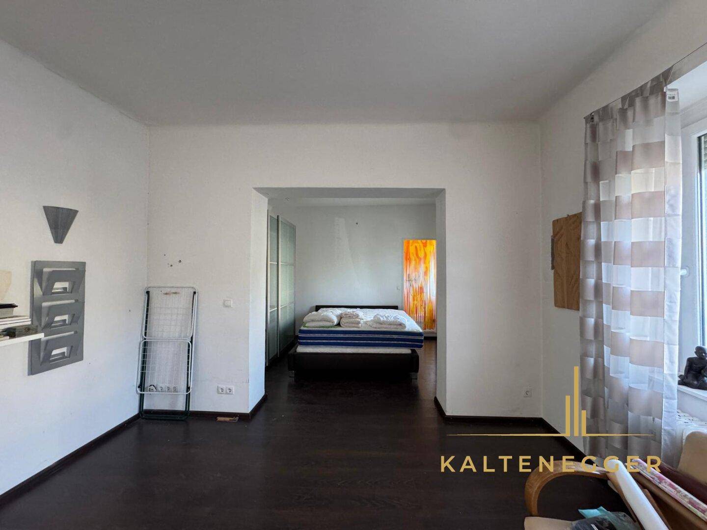Schlafzimmer mit dunklem Holzboden und offenem Übergang zu einem weiteren Raum.