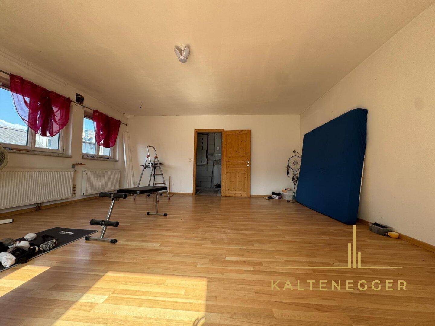 Großer, heller Raum mit Holzboden und Fenstern, ideal als Wohn- oder Hobbyraum.