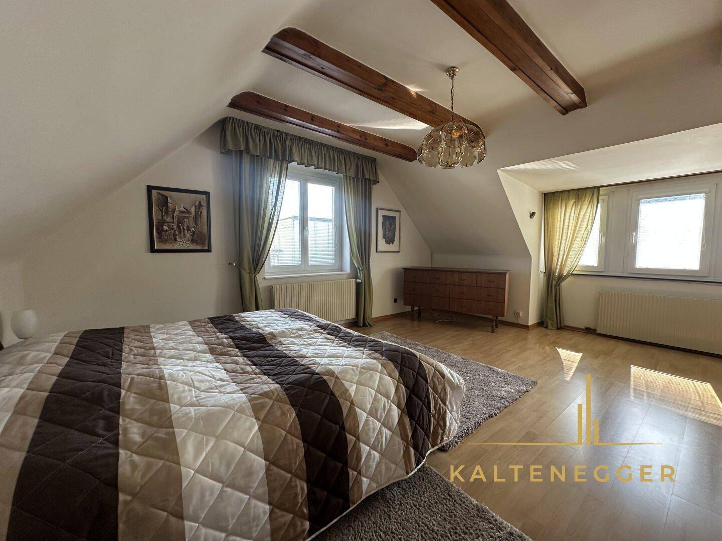 Gemütliches Schlafzimmer mit Holzbalken, Parkettboden und zwei Fenstern für natürliche Belichtung.