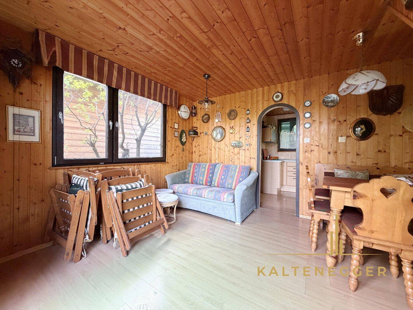 Gemütlicher Wohnbereich mit Holztäfelung, Sofa und Blick auf den Essbereich und die Küche.