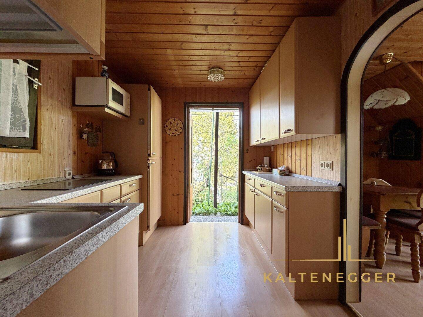 Helle Küche mit Holzschränken, Arbeitsplatten und direktem Zugang zum Garten.
