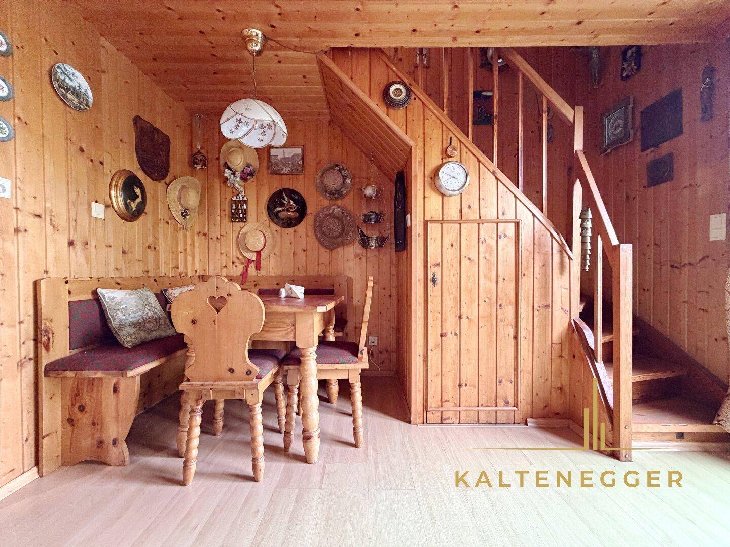 Rustikaler Wohn- und Essbereich mit Holztäfelung, traditionellen Möbeln und einer Holztreppe.