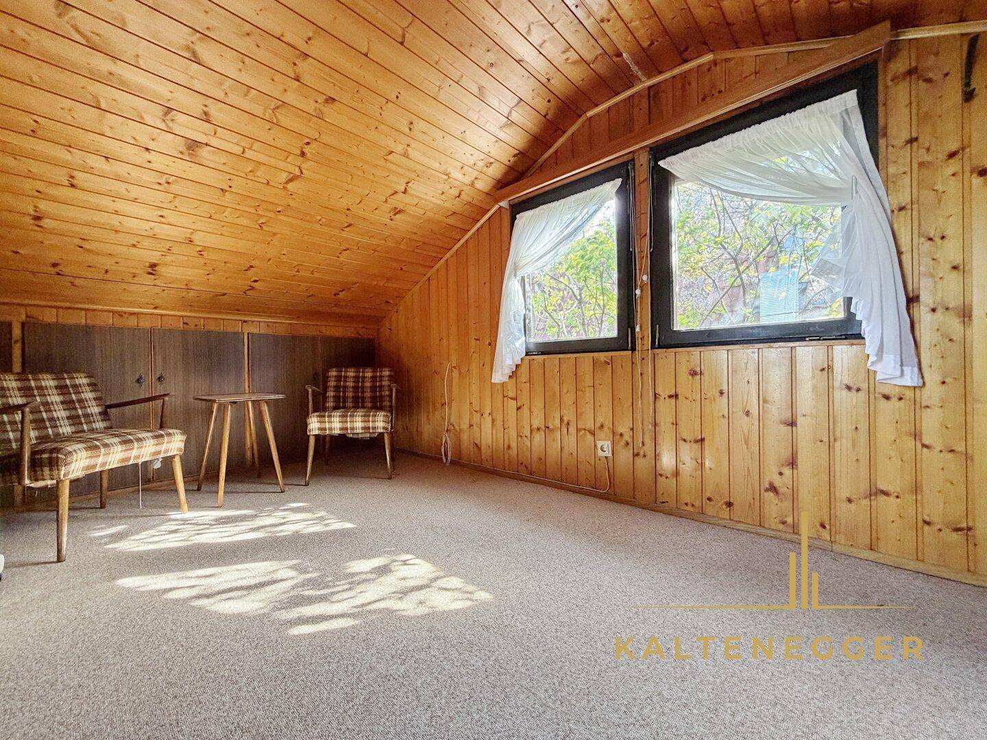 Geräumiges Schlafzimmer im Dachgeschoss mit Teppichboden, Holzvertäfelung und zwei Fenstern.