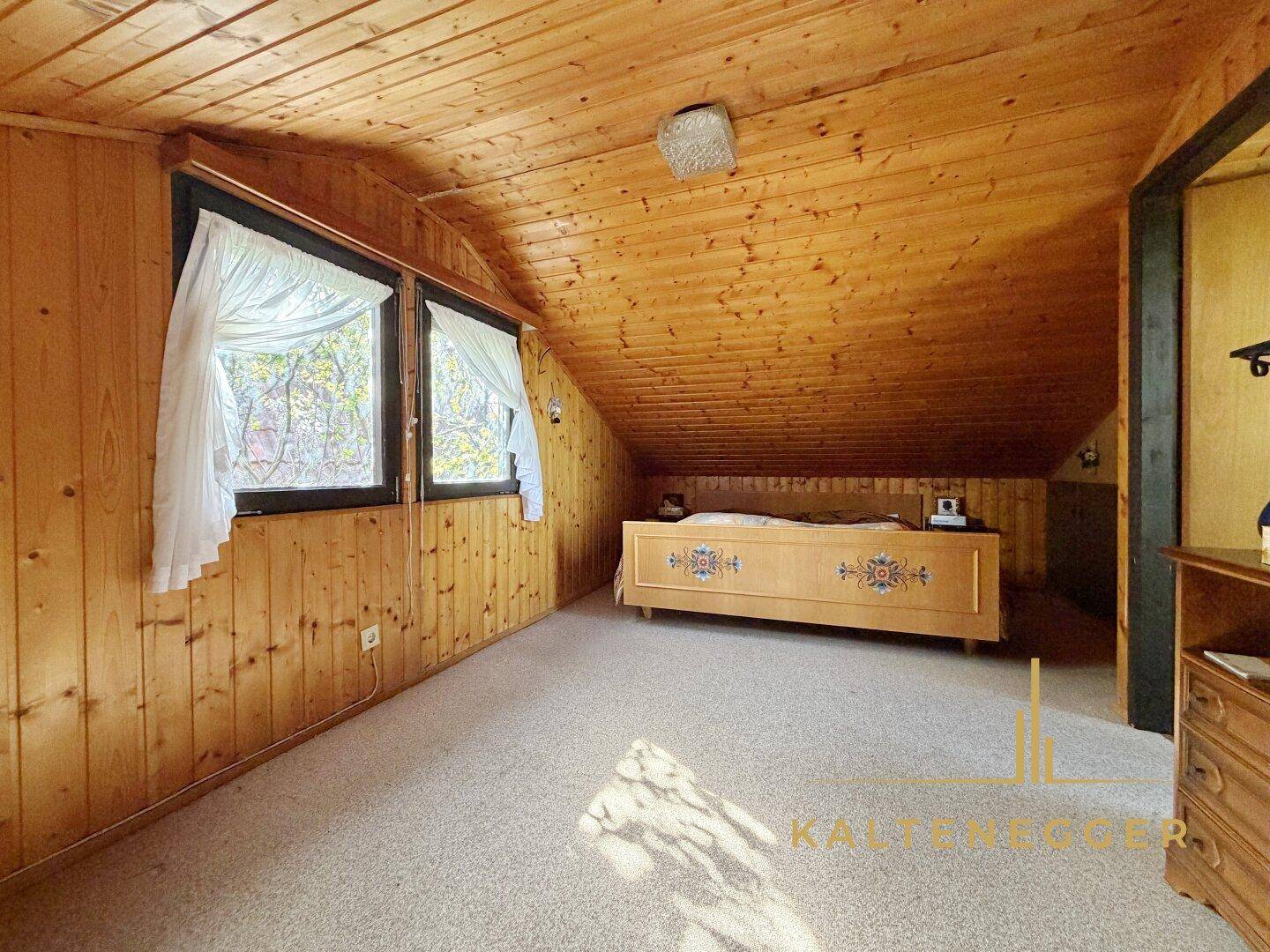 Gemütliches Schlafzimmer im Dachgeschoss mit Holzbett, Teppichboden und schrägen Wänden.