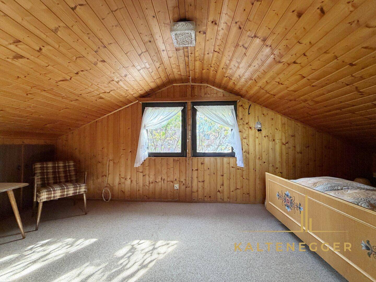 Helles Schlafzimmer im Dachgeschoss mit traditionellem Bett, Teppichboden und Holzvertäfelung.