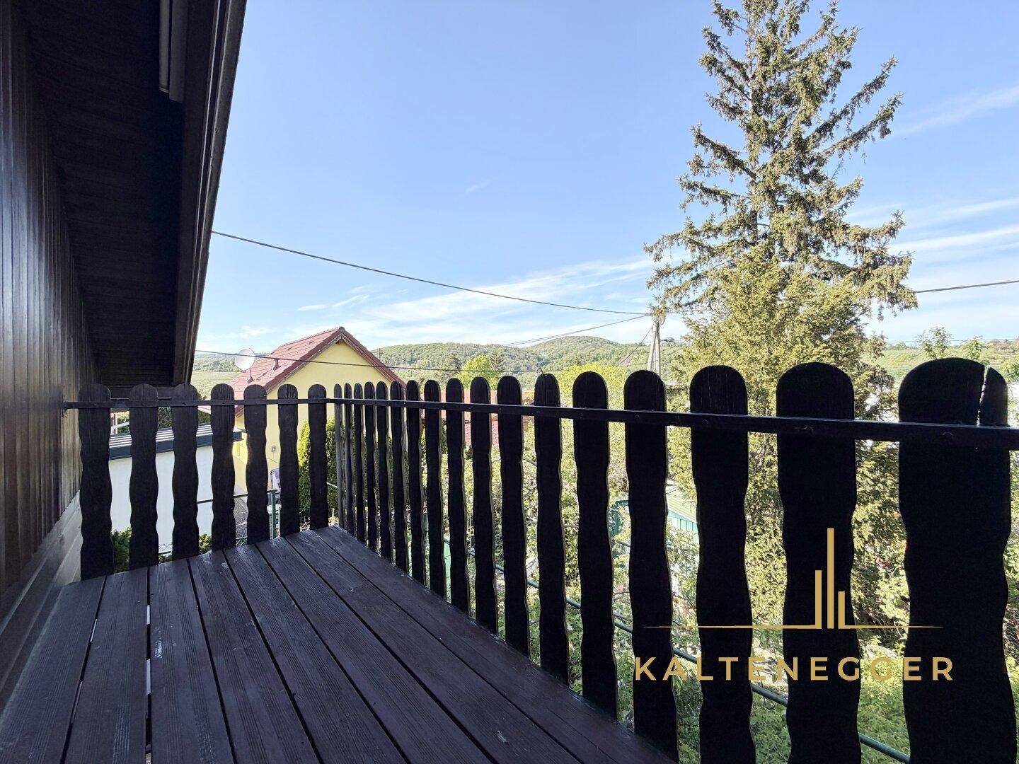 Sonniger Holzbalkon mit weitem Blick über die umliegende Landschaft und Häuser.