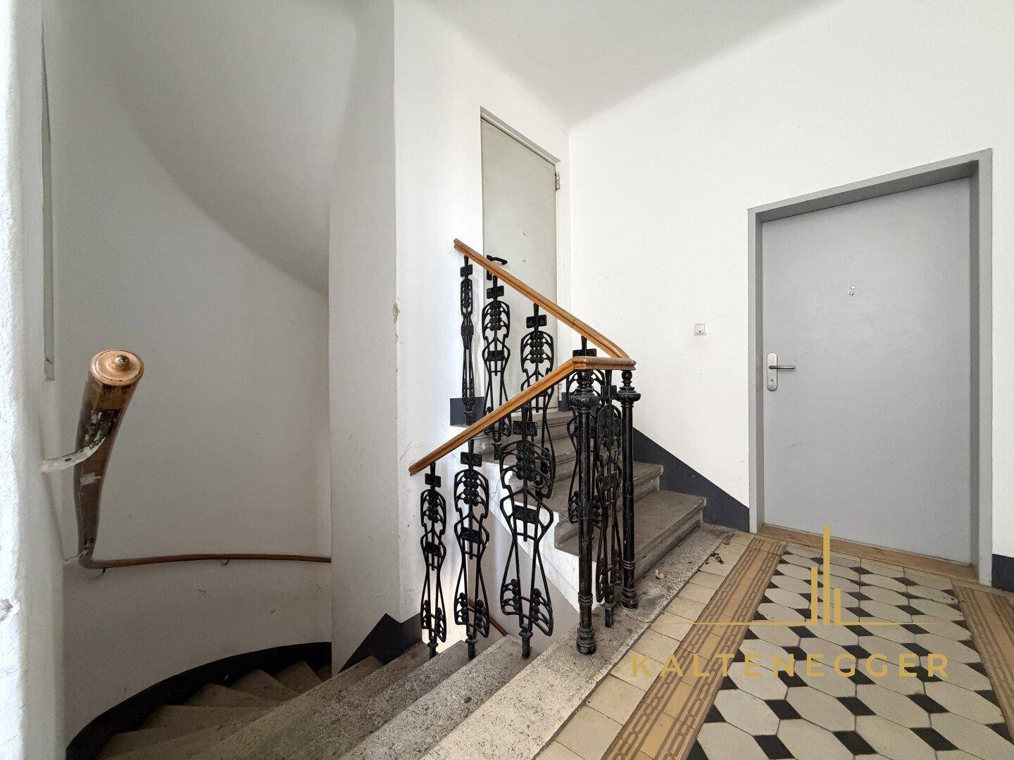 Historisches Treppenhaus mit schmiedeeisernem Geländer und gemustertem Fliesenboden.