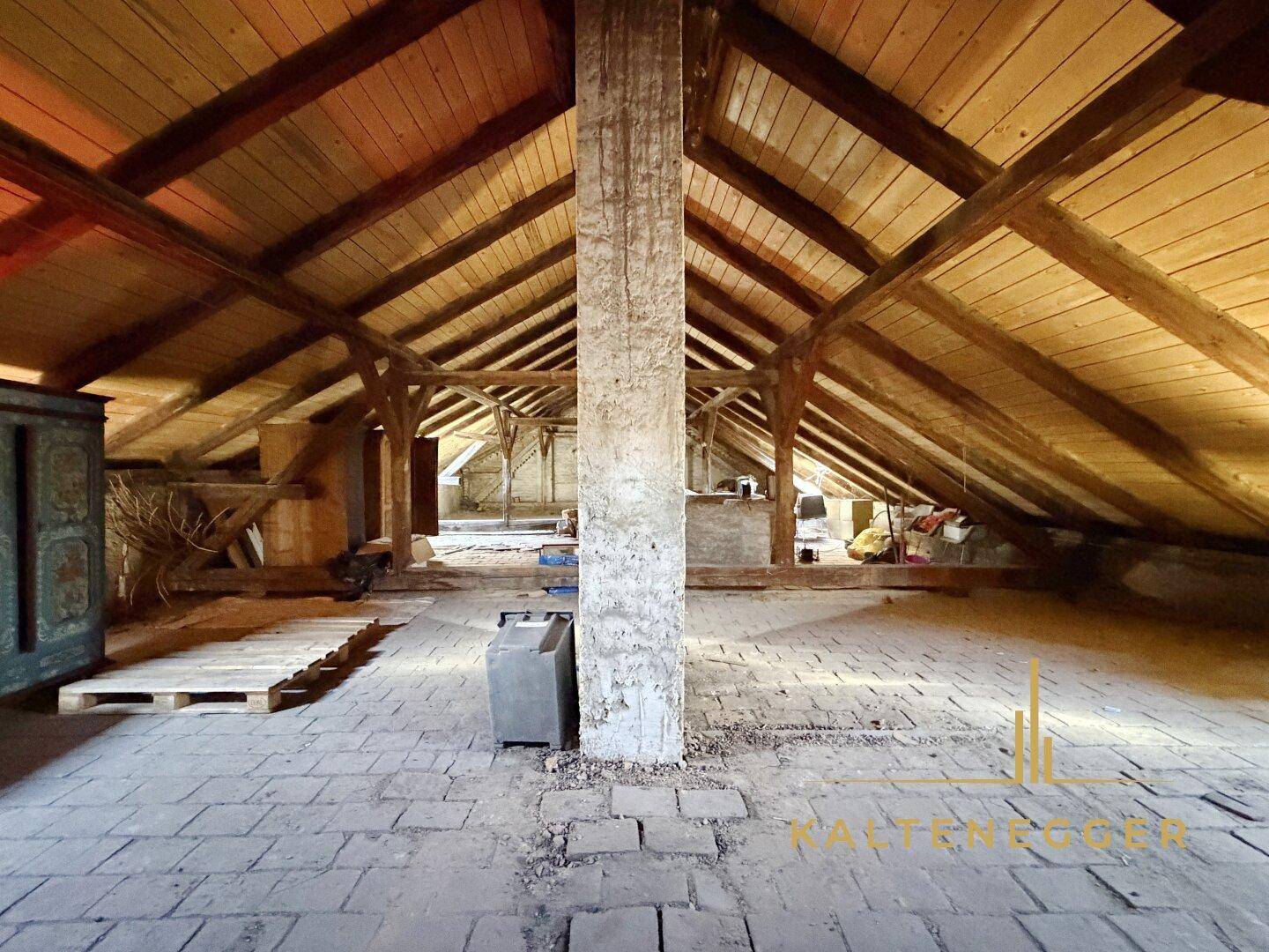 Geräumiger Dachboden mit sichtbaren Holzbalken und Ziegelboden, bereit für den Ausbau.