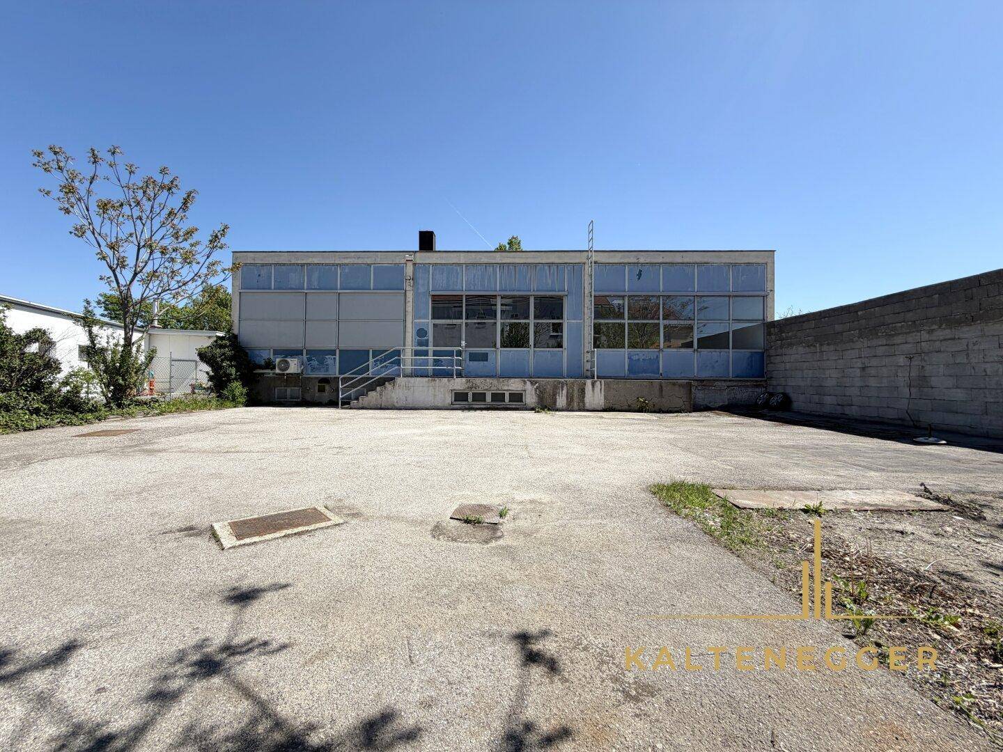 Gewerbegebäude mit großer Glasfassade und weitläufiger, gepflasterter Freifläche davor.
