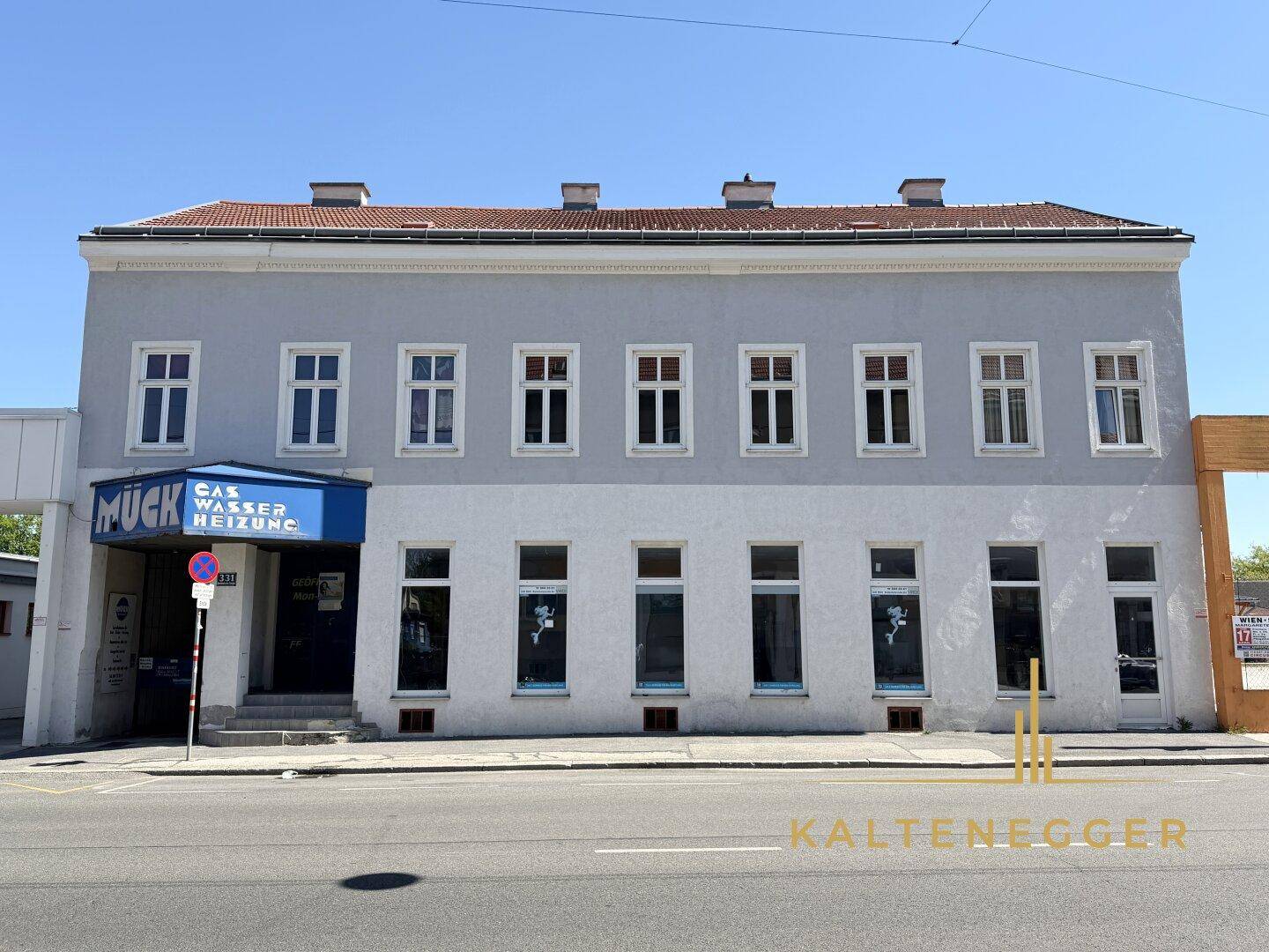 Vorderansicht eines Mehrfamilienhauses mit hellgrauer Fassade und vielen Fenstern an einem sonnigen Tag.