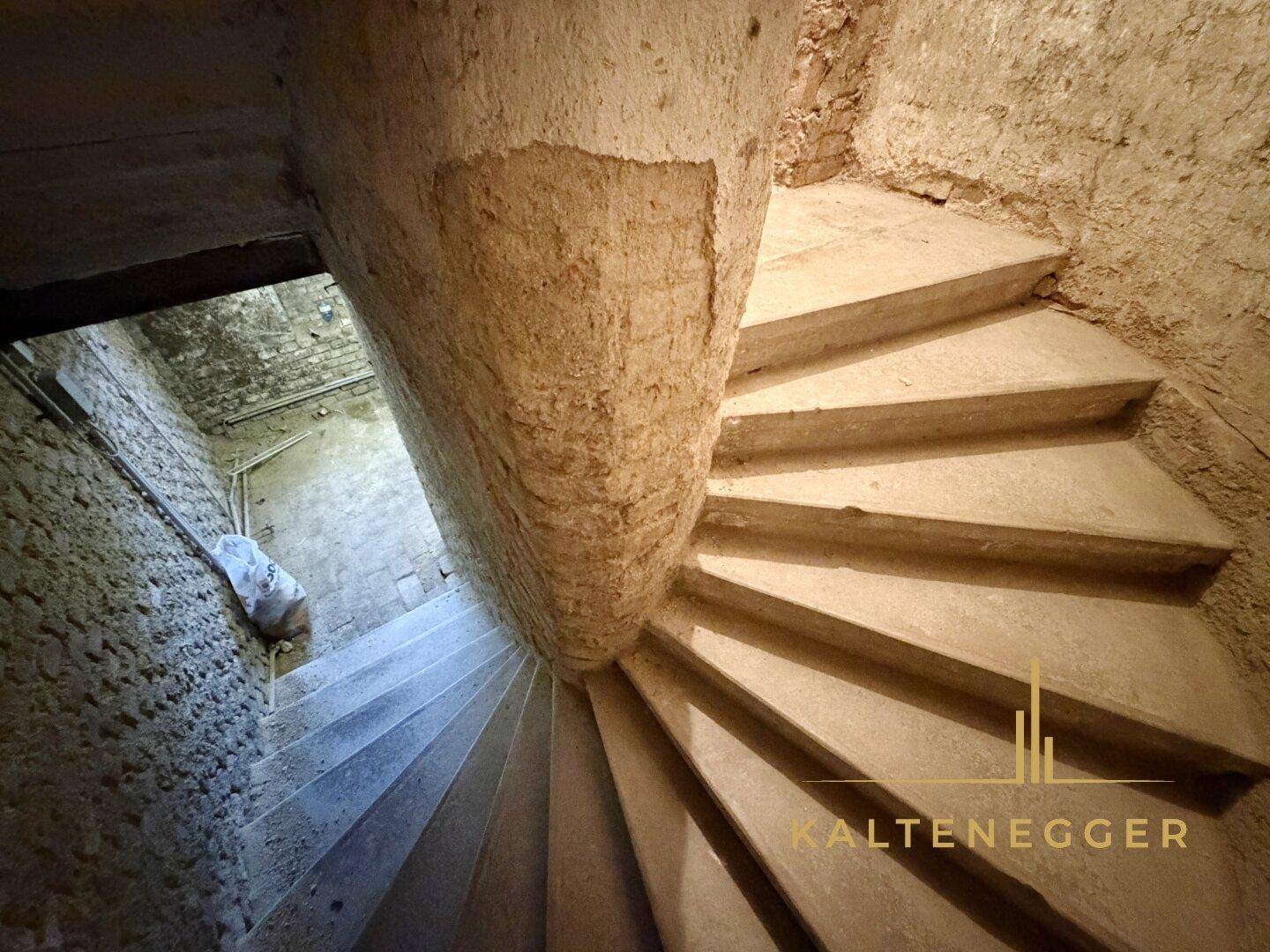 Alte Wendeltreppe führt in einen Kellerraum mit rauen Steinwänden.