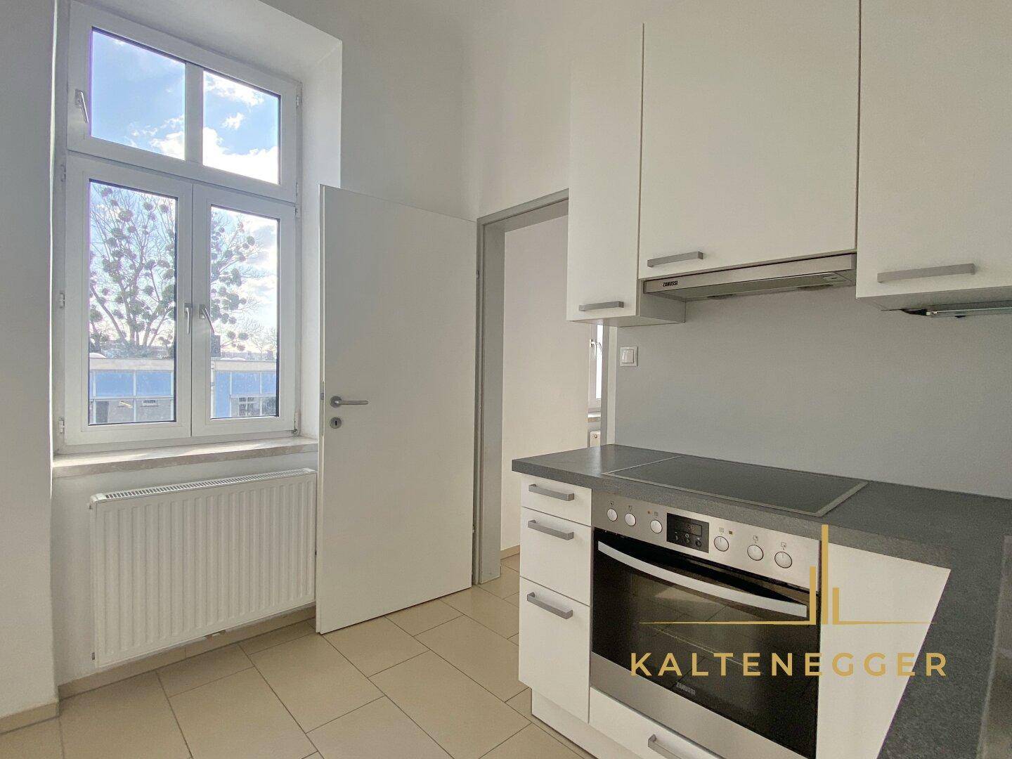 Helle Küche mit Einbauschränken, Fenster und Blick nach draußen.