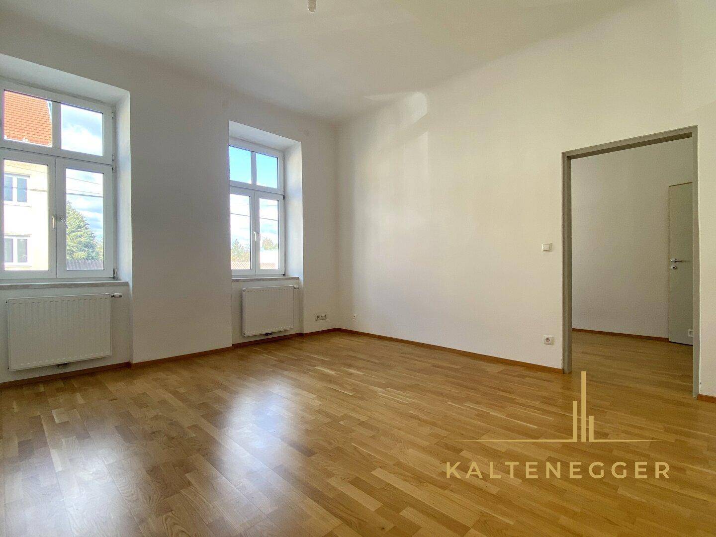 Helles Wohnzimmer mit zwei großen Fenstern und Parkettboden, frisch gestrichen.