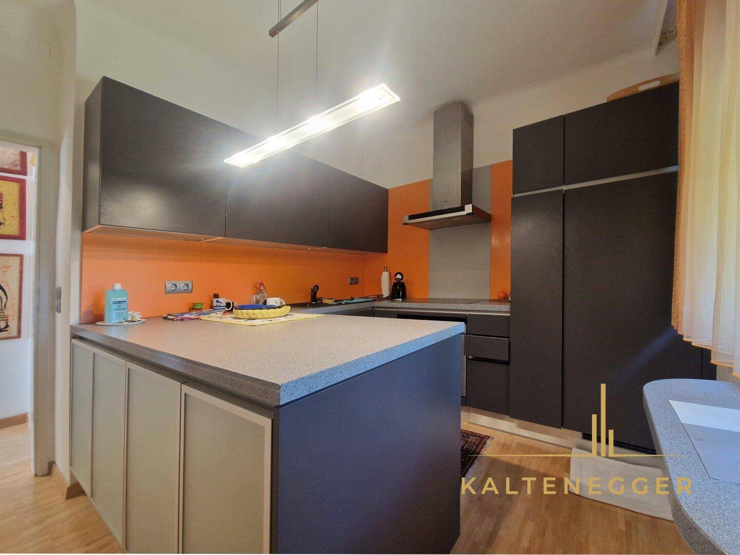 Moderne Küche mit dunklen Schränken, orangefarbener Rückwand und integrierter Dunstabzugshaube.