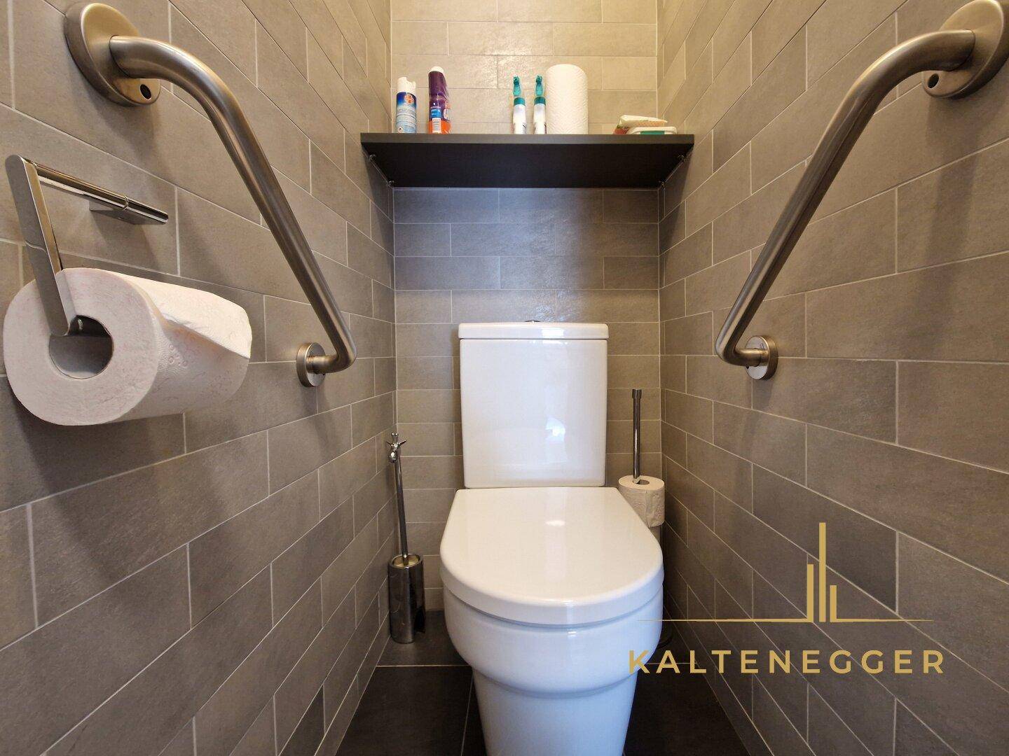 Separate Toilette mit modernen Fliesen und Haltegriffen für zusätzliche Sicherheit.