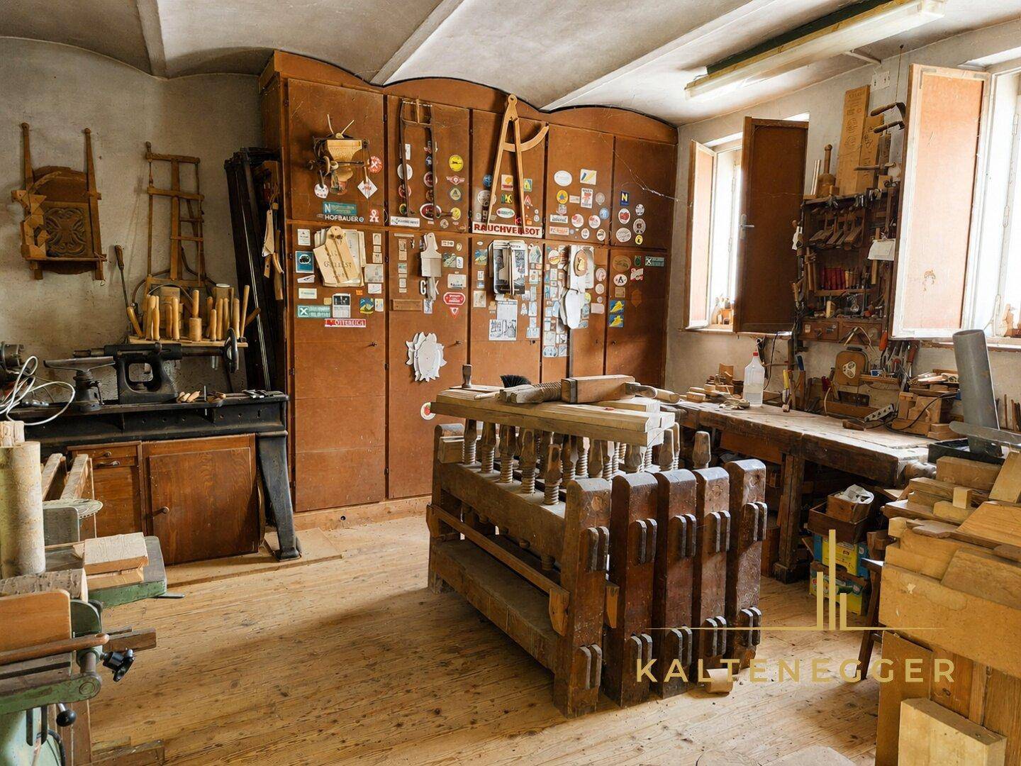 Geräumige Holzwerkstatt mit vielen Werkzeugen, Holzmaterialien und hohen Fenstern.