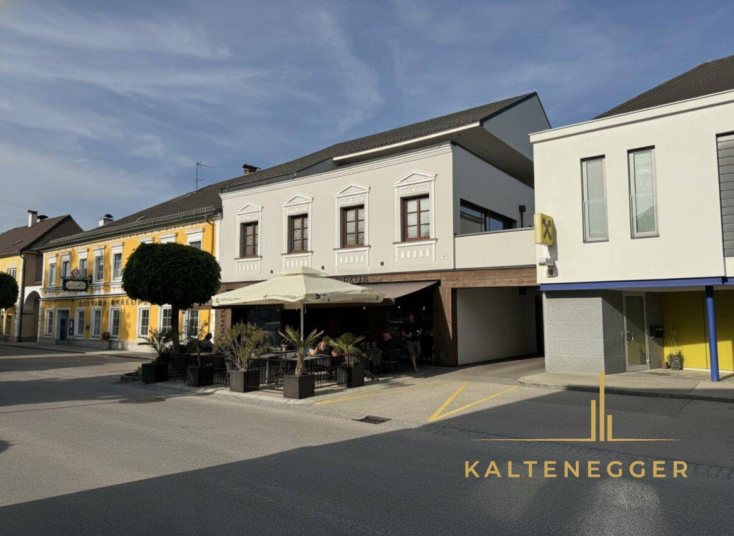 Seitenansicht des Gebäudes mit moderner Erweiterung und angrenzendem älteren Bauwerk an der Straße.
