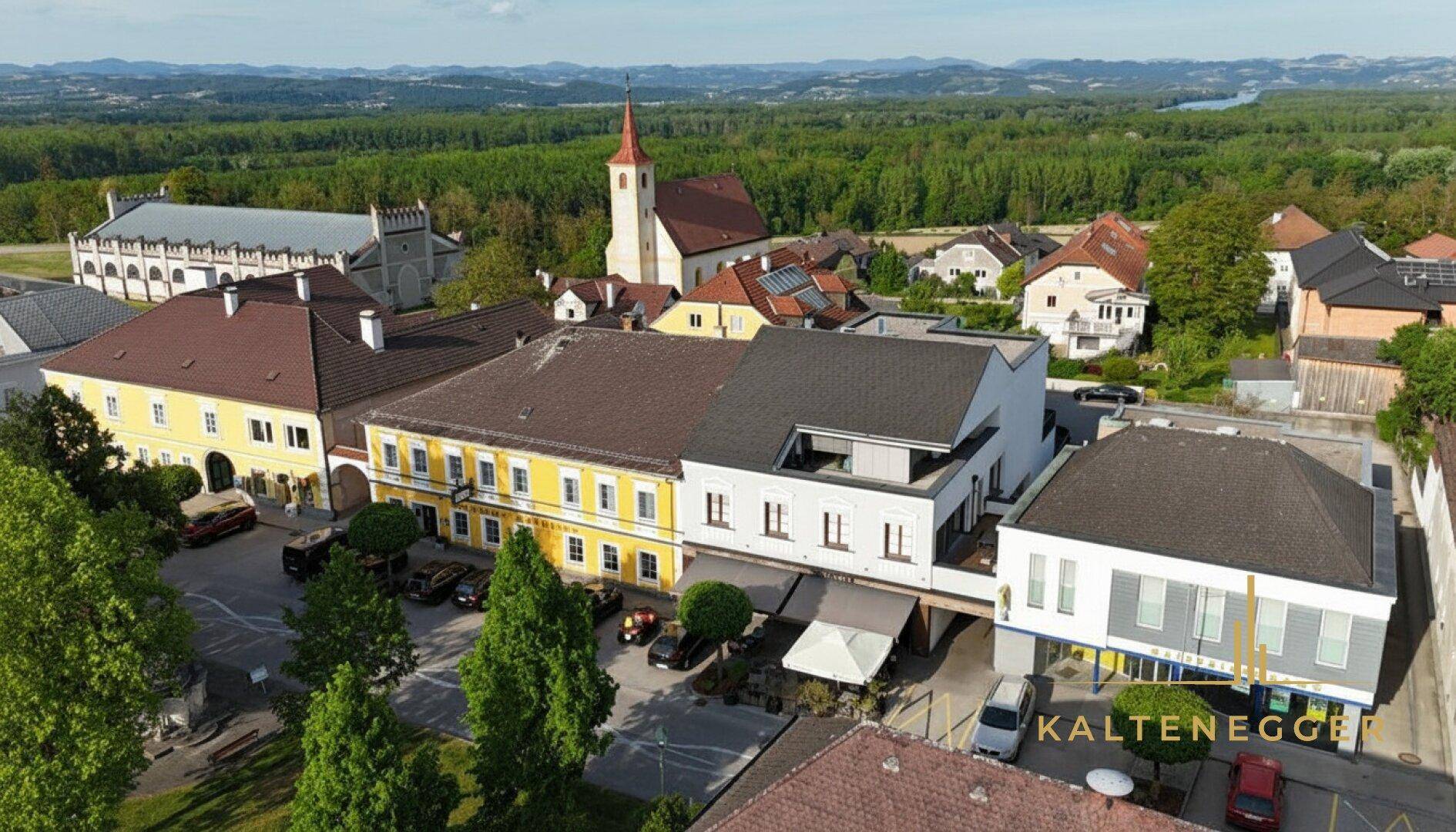 Luftaufnahme der Ortschaft mit dem Anwesen, umgeben von grüner Landschaft und einem Fluss im Hintergrund.