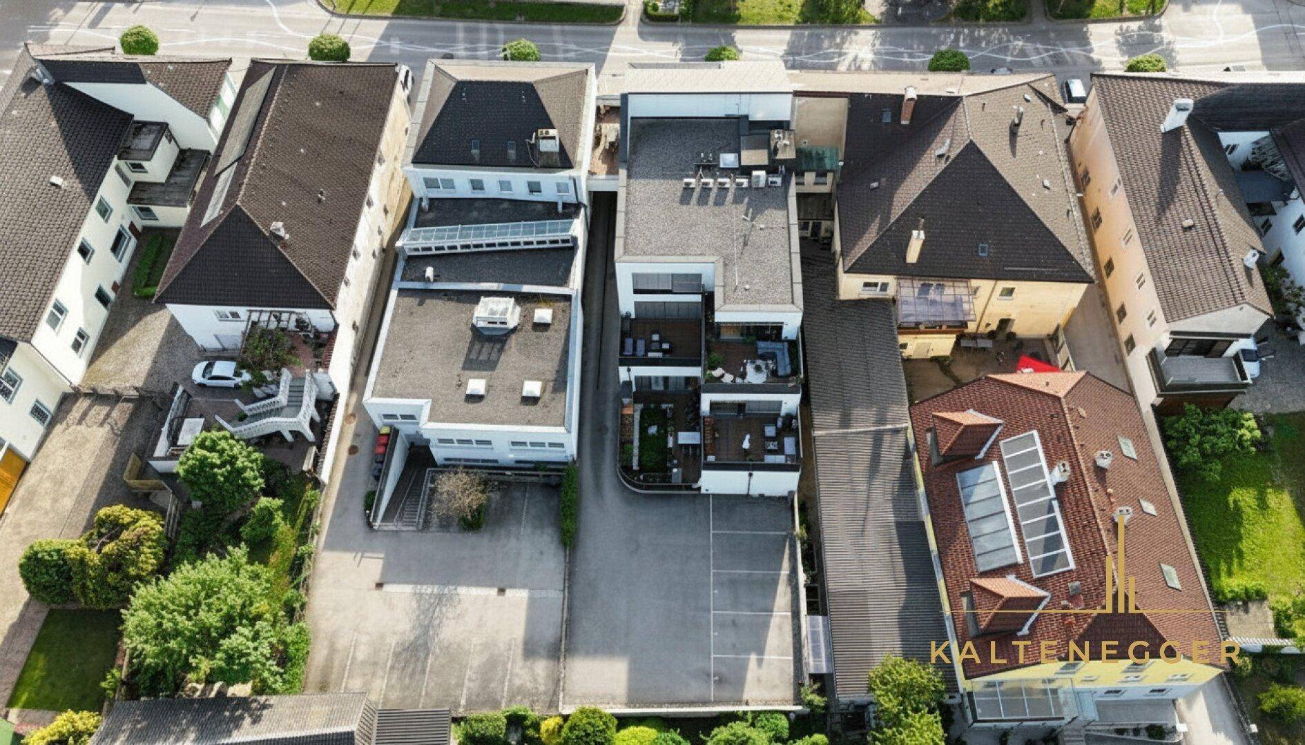 Draufsicht auf das Anwesen mit Flachdach, Terrassen und Parkplätzen, umgeben von weiteren Gebäuden.