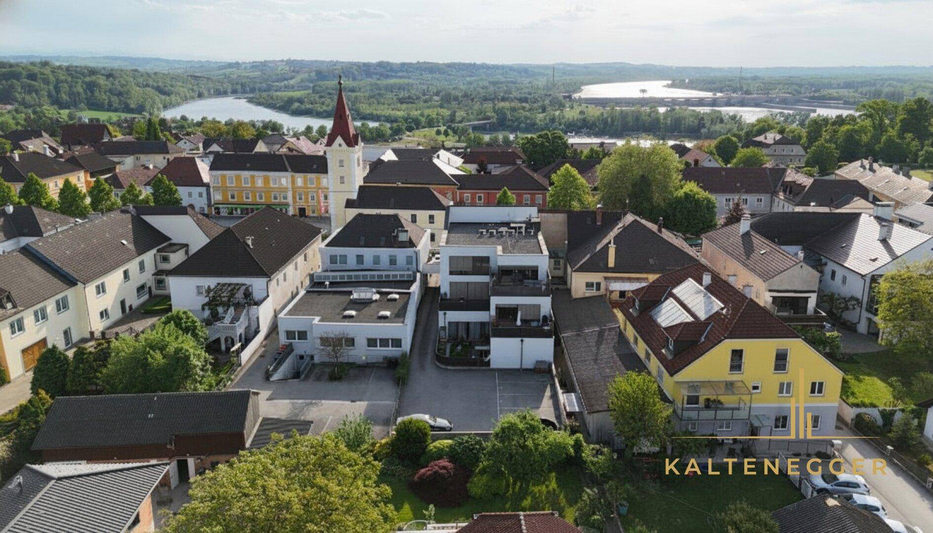 Panoramische Luftaufnahme der Stadt mit dem Anwesen, Fluss und Kirche, eingebettet in eine grüne Landschaft.