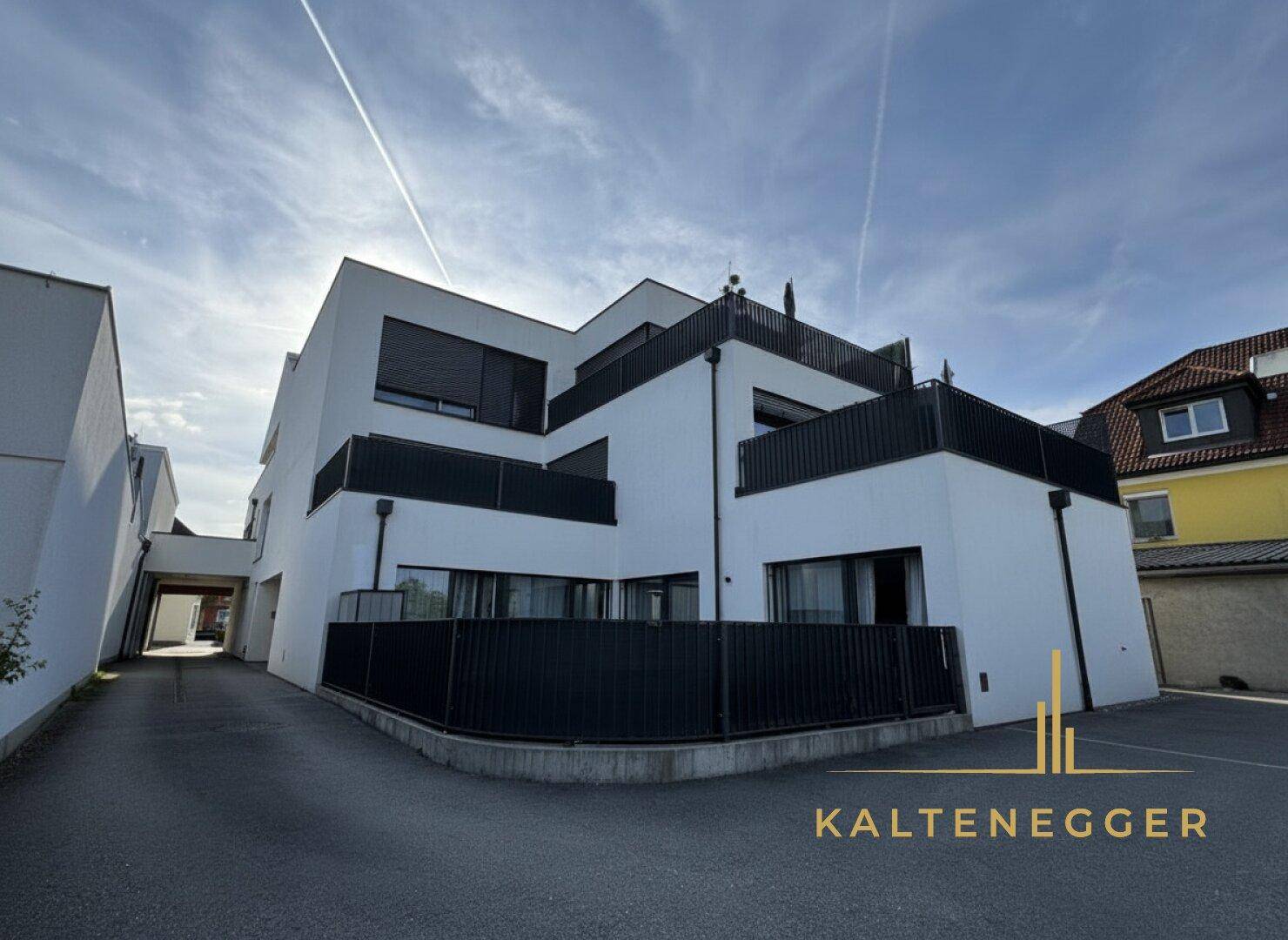 Rückansicht des modernen Gebäudes mit mehreren Balkonen und Terrassen unter einem sonnigen Himmel.