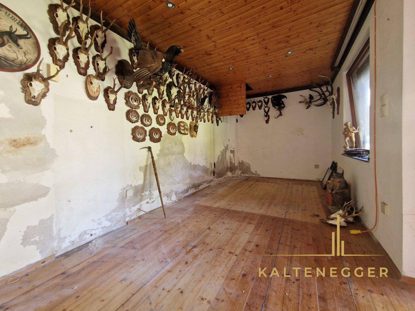 Rustikaler Raum mit Holzboden, Holzdecke und zahlreichen Jagdtrophäen an den Wänden.