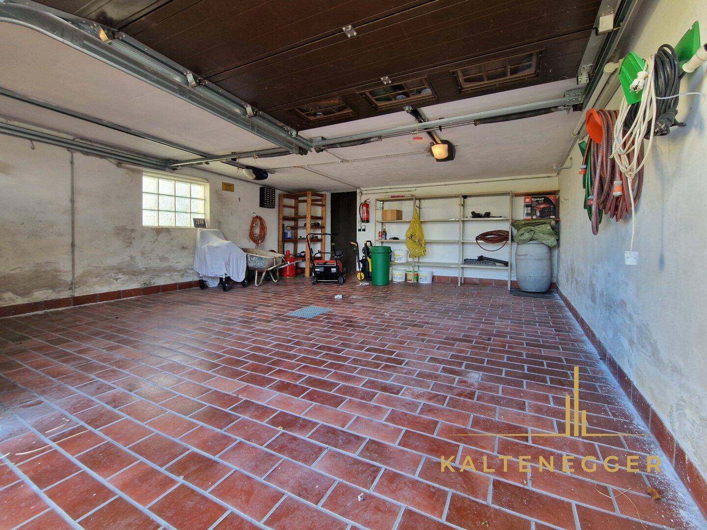 Geräumige Garage mit Ziegelboden, Regalen und ausreichend Stauraum für Werkzeuge.
