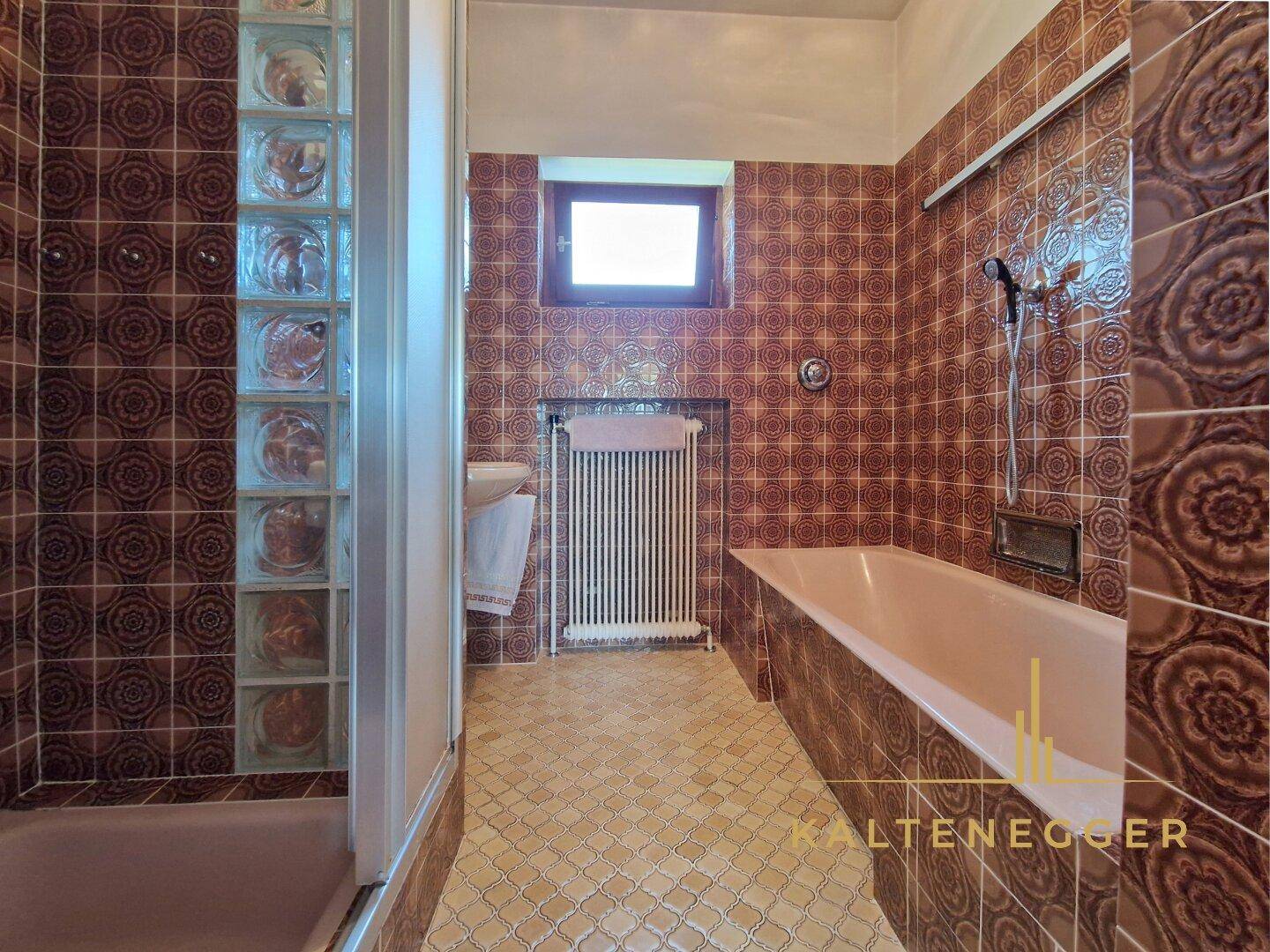 Badezimmer im Stil der 80er Jahre mit braunen Fliesen, Badewanne und Duschbereich.