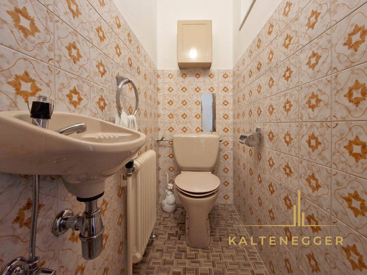 Kleines Gäste-WC mit gemusterten Fliesen, Waschbecken und Toilette im Retro-Stil.
