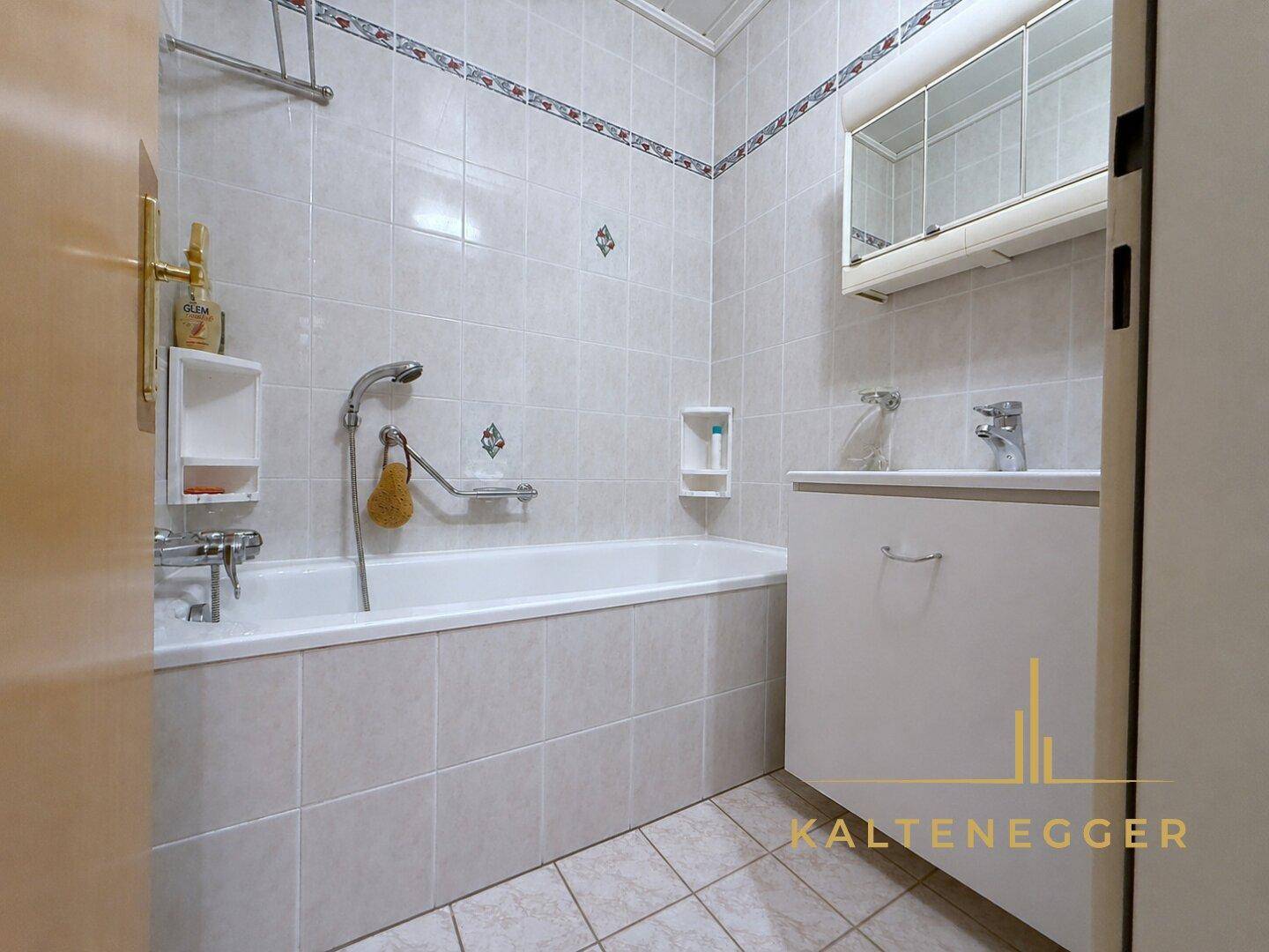 Gefliestes Badezimmer mit Badewanne und Duschvorrichtung, praktisch und funktional.