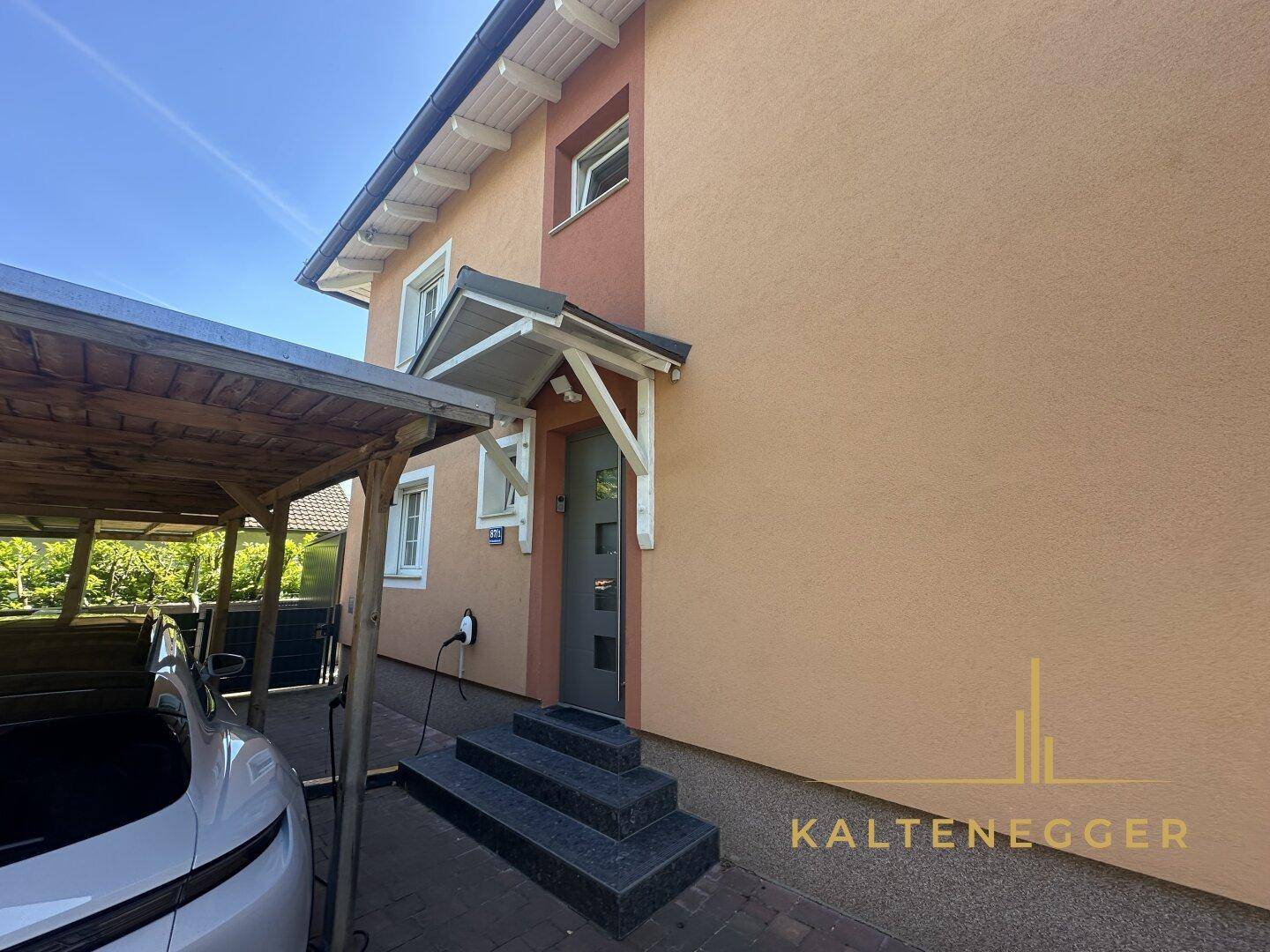 Eingangsbereich des Hauses mit Carport und einer Ladestation für Elektrofahrzeuge.