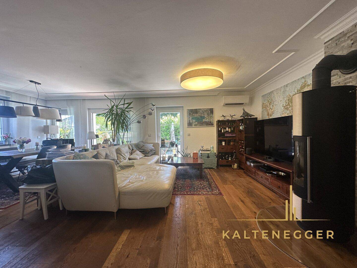 Heller Wohnbereich mit Holzboden, großem Sofa, Kaminofen und Zugang zum Garten.