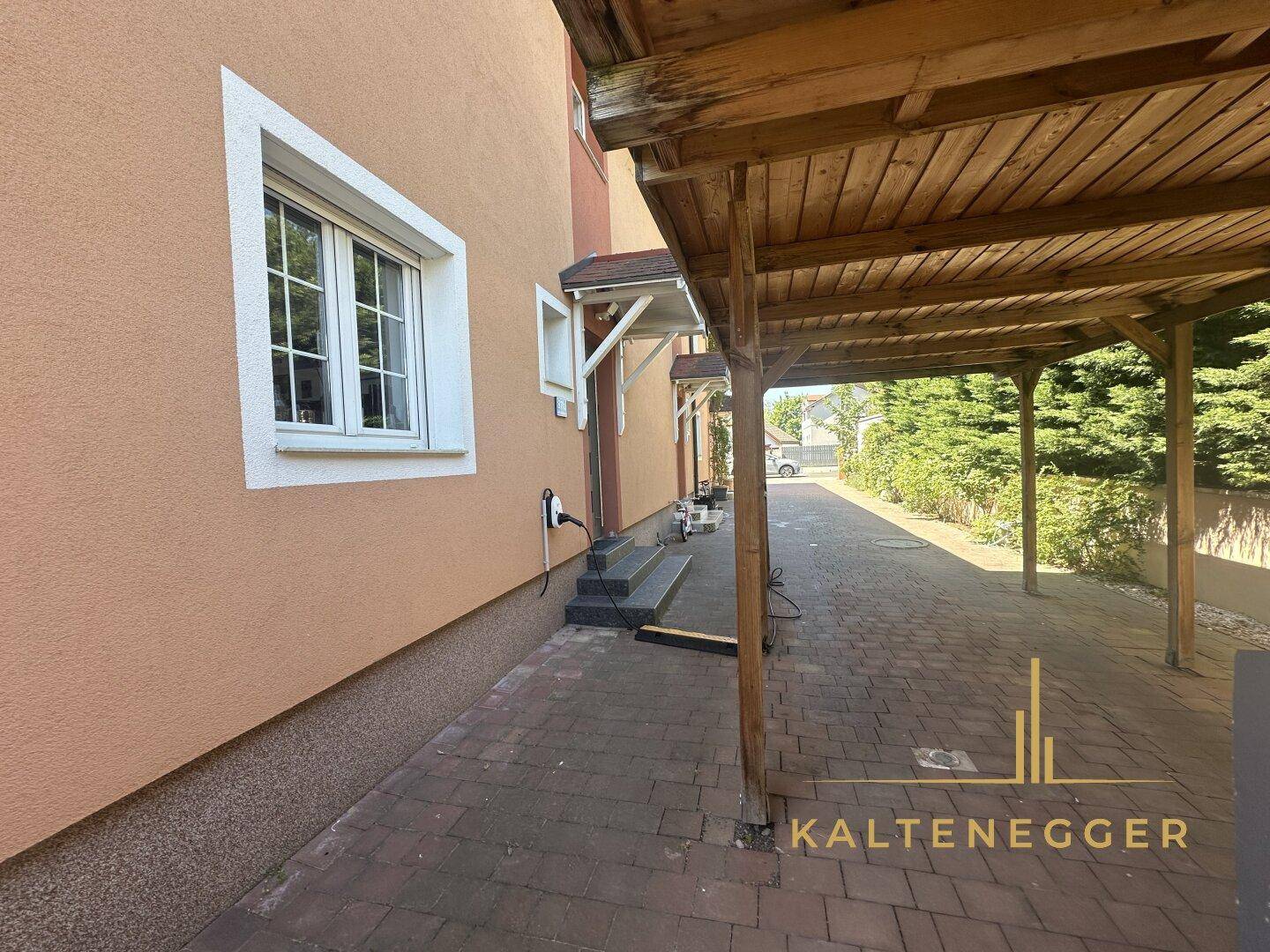 Einfahrt mit Carport und gepflastertem Bereich neben dem Haus.