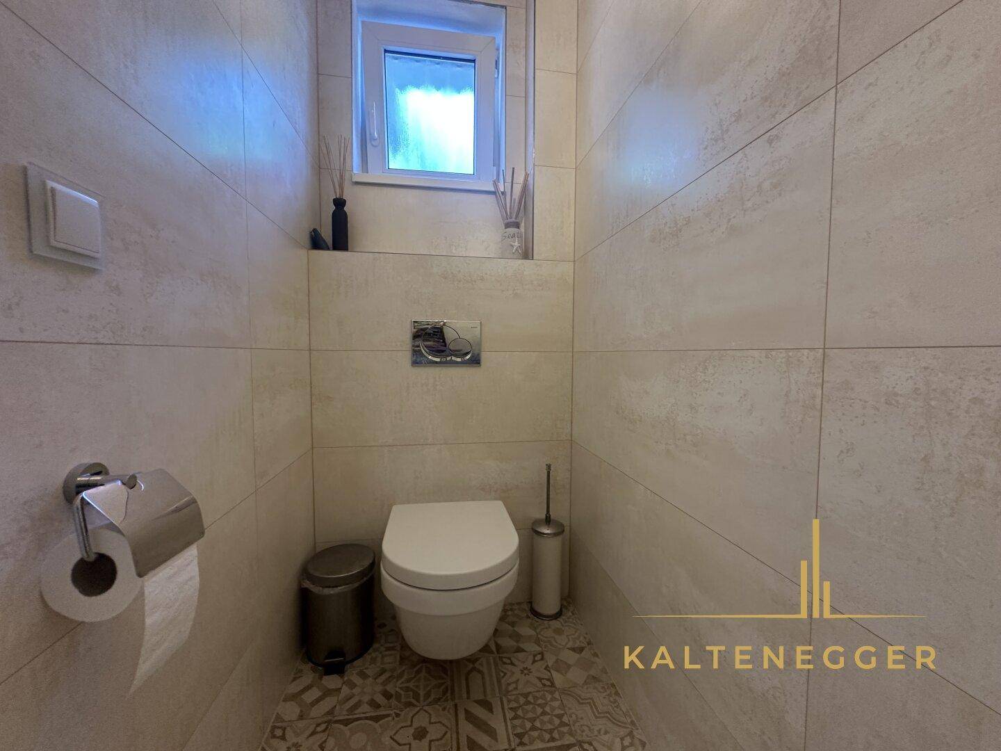 Modernes Gäste-WC mit Wand-WC, Fliesenboden und kleinem Fenster.