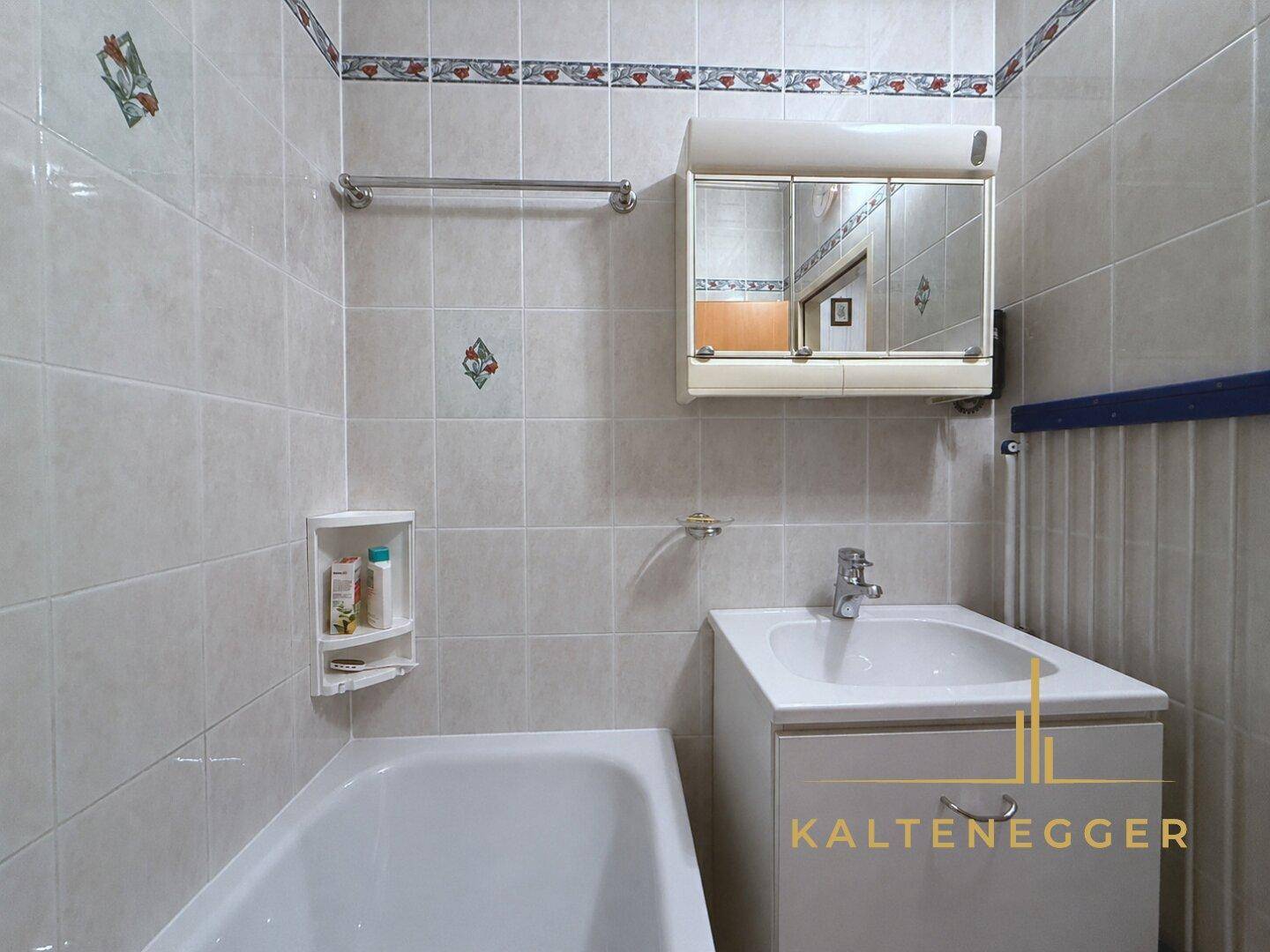 Badezimmer mit Badewanne, Waschbecken und Spiegelschrank, komplett gefliest.