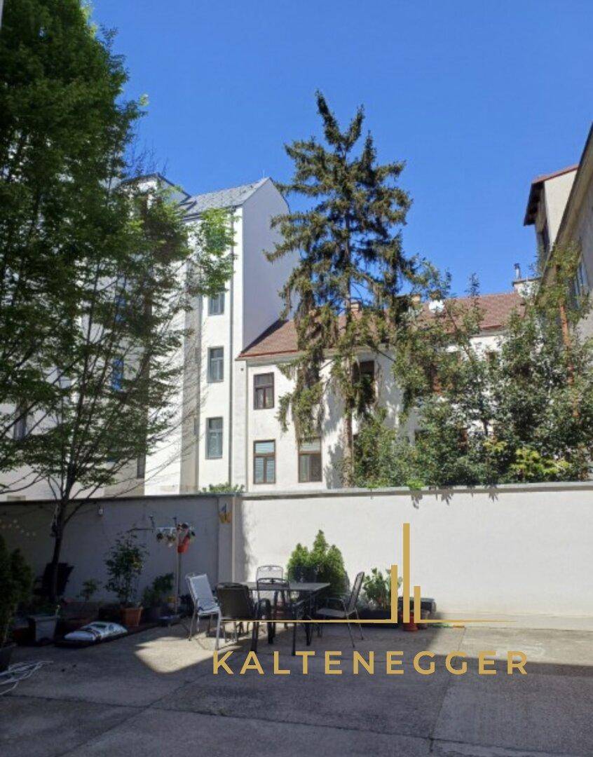 Gemütliche Terrasse mit Sitzgelegenheiten im Freien, umgeben von Grün und Gebäuden.