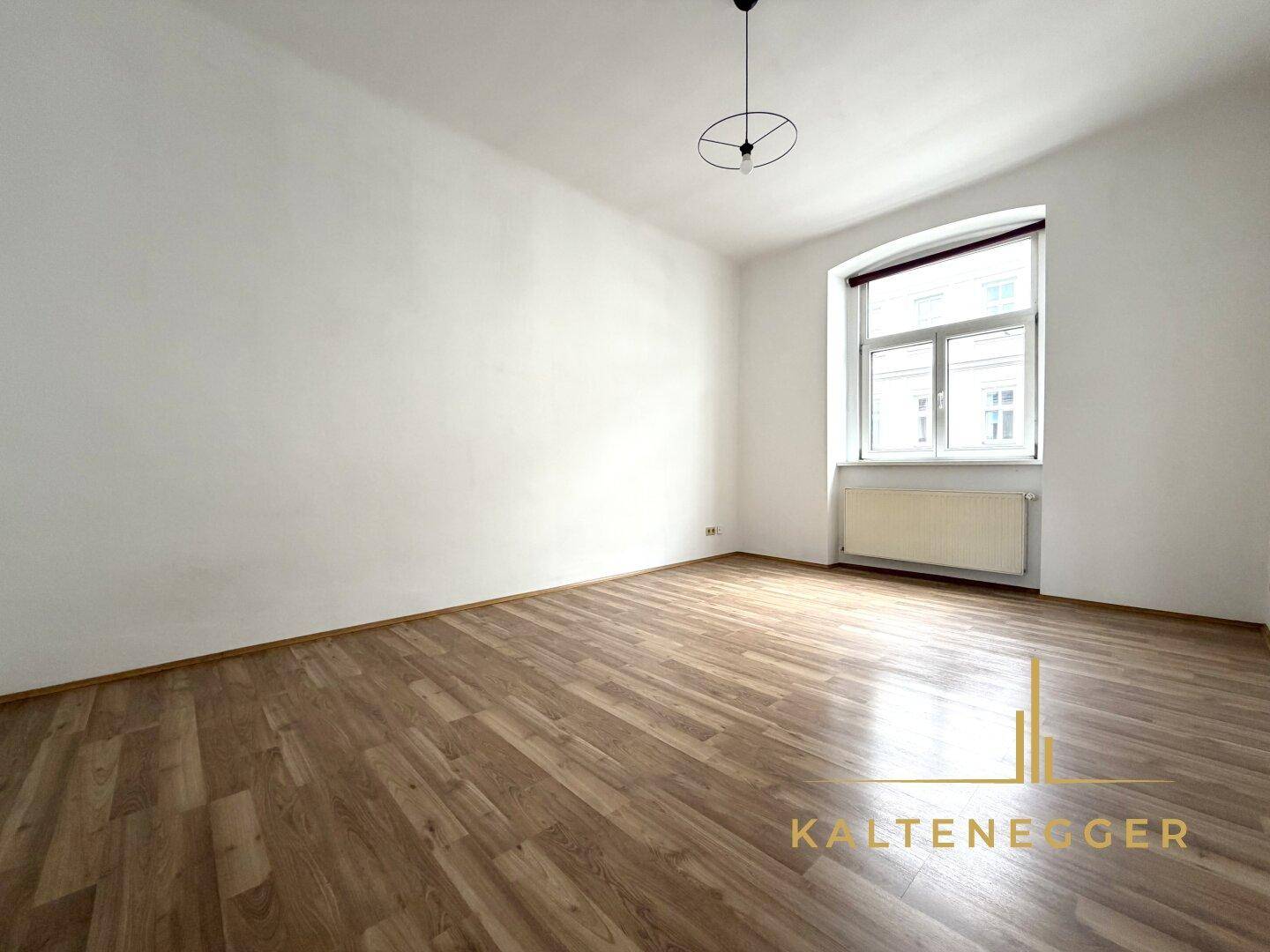 Heller, leerer Raum mit Holzparkettboden und einem Fenster, das natürliches Tageslicht hereinlässt.