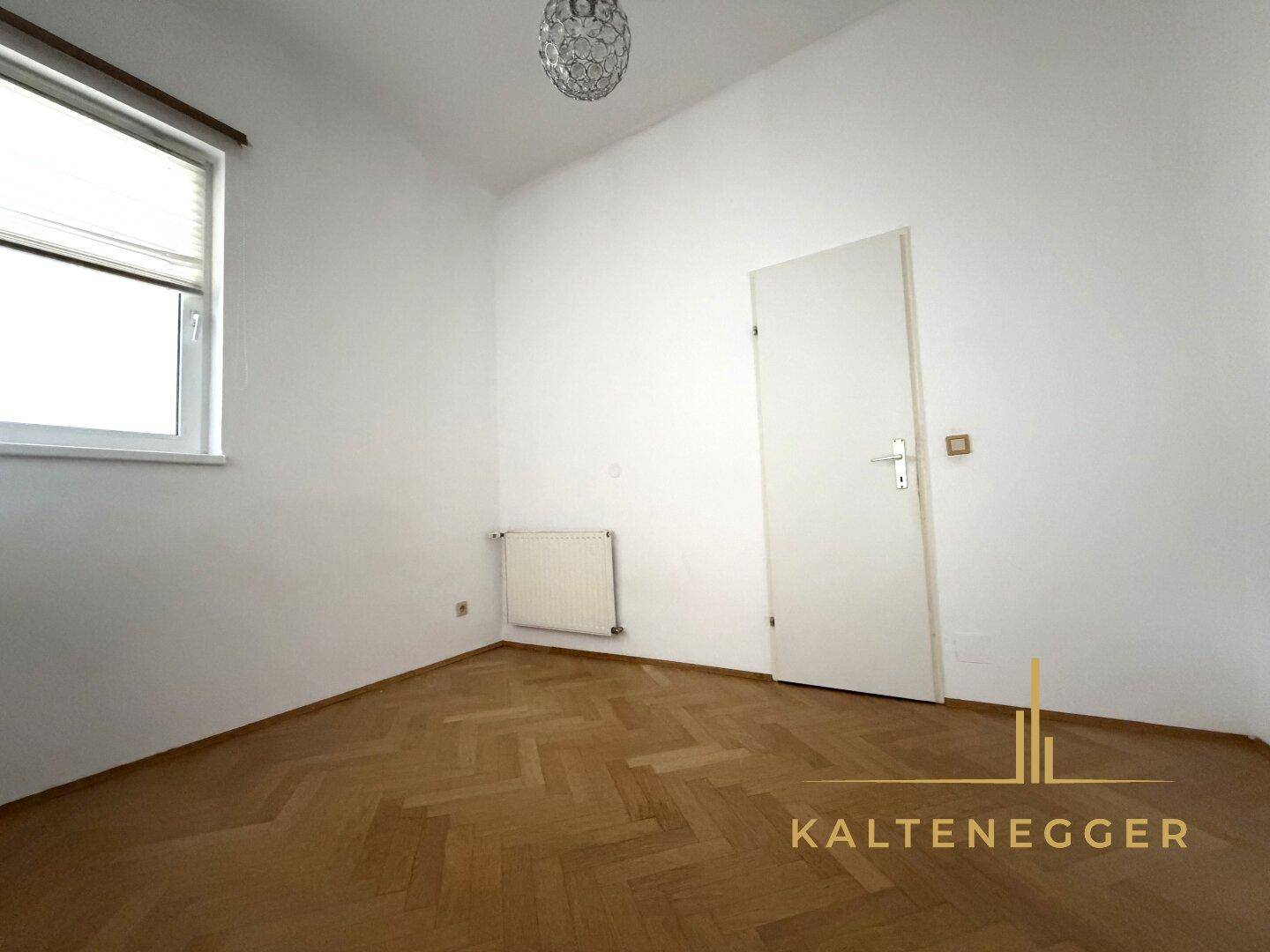 Leeres Zimmer mit Fischgrätparkett, weiß gestrichenen Wänden und einem Fenster für natürliches Licht.